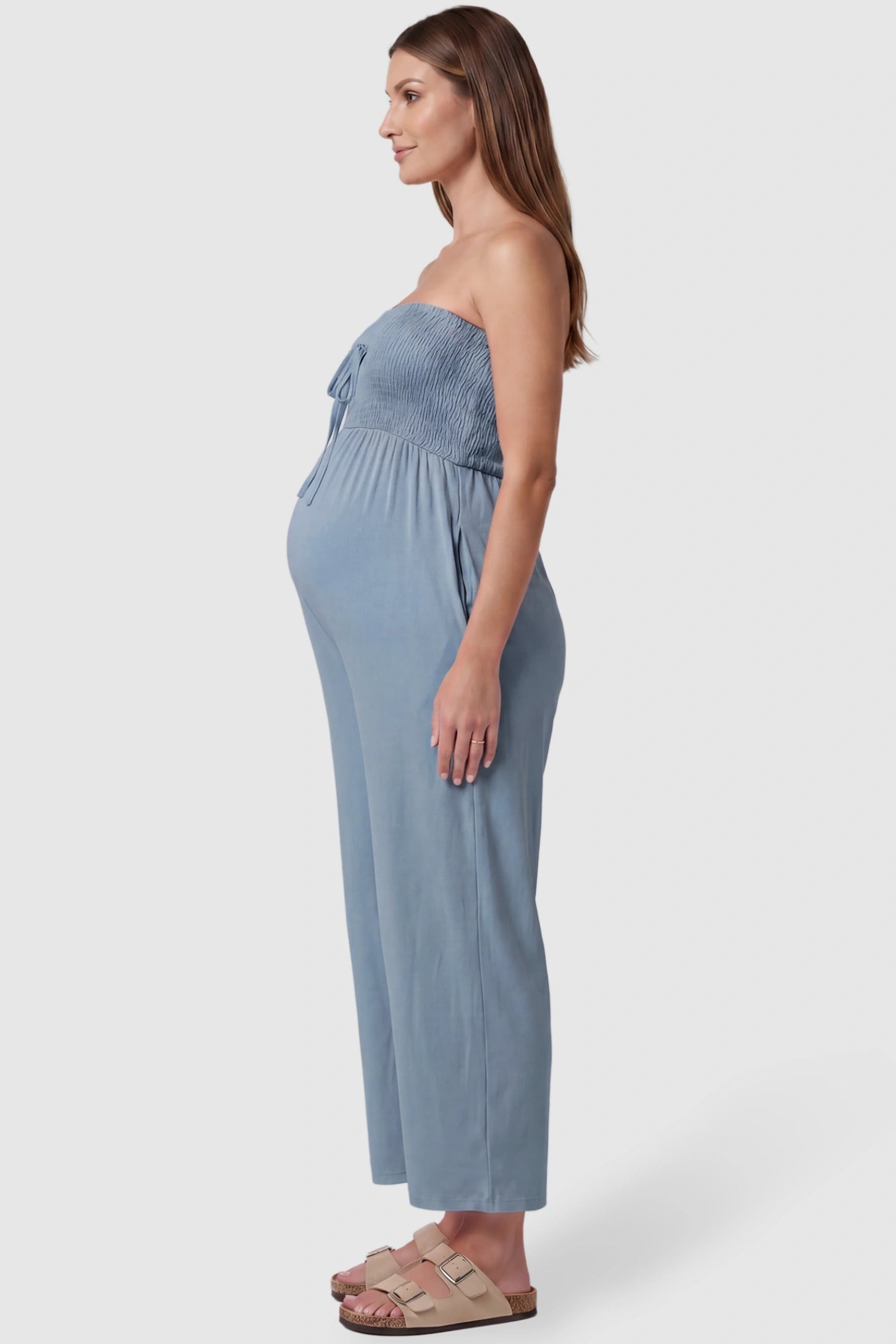Strapless Smocked Bust Wide Leg Maternity Jumpsuit Strapless Smocked Bust Wide Leg Maternity Jumpsuit in Blue featuring a relaxed leg design on a pregnant model, side view.