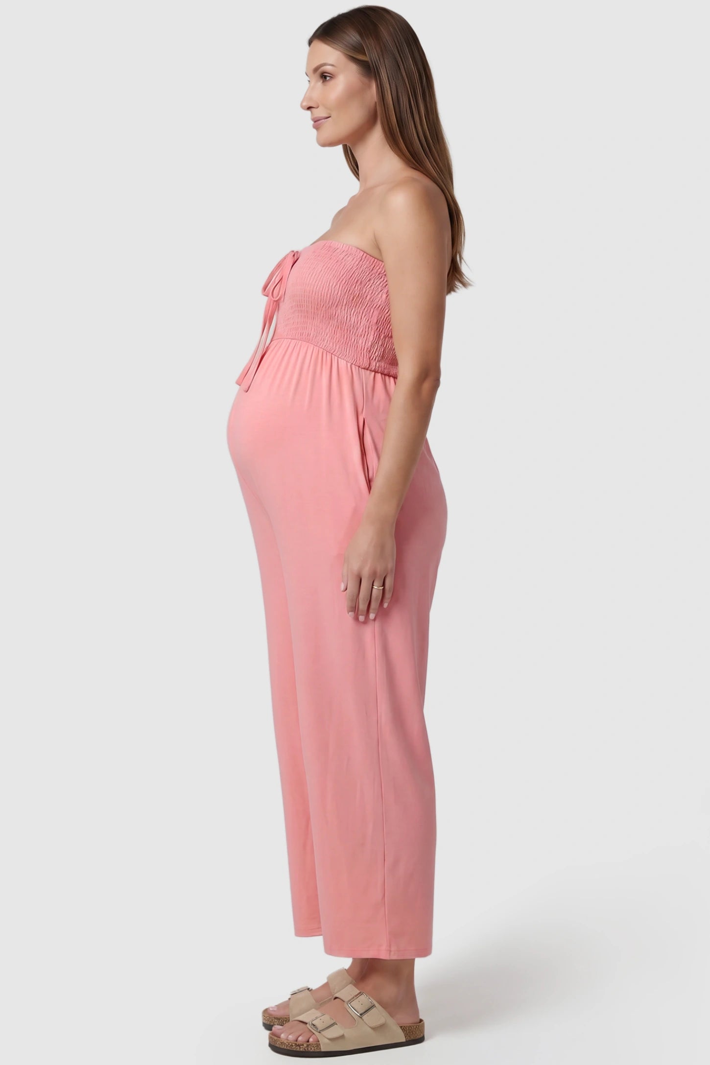 Strapless Smocked Bust Wide Leg Maternity Jumpsuit Strapless Smocked Bust Wide Leg Maternity Jumpsuit in Pink featuring a relaxed leg design on a pregnant model, side view.