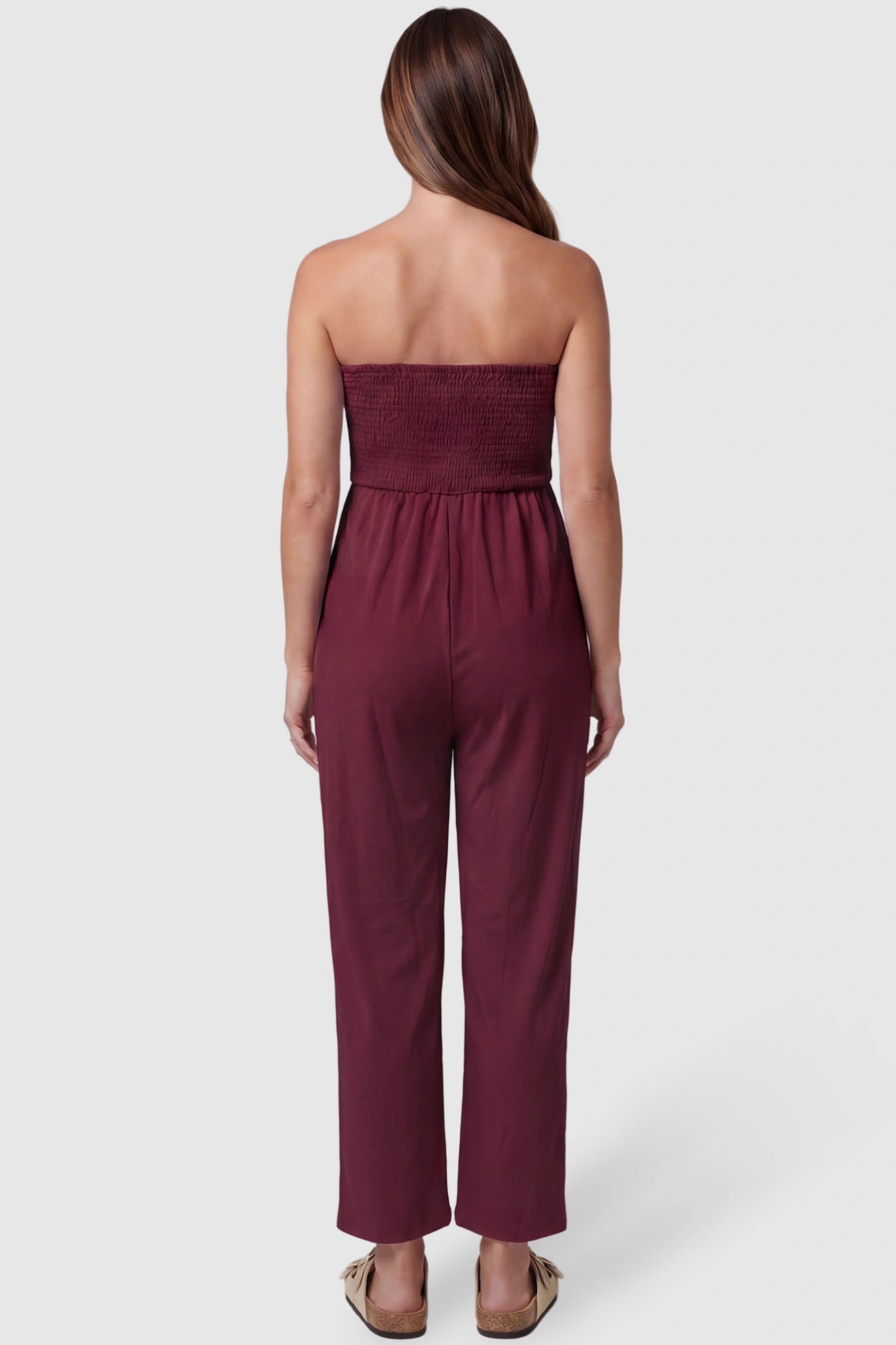 Strapless Smocked Bust Wide Leg Maternity Jumpsuit Strapless Smocked Bust Wide Leg Maternity Jumpsuit in Wine Red featuring a relaxed leg design on a pregnant model, back view.