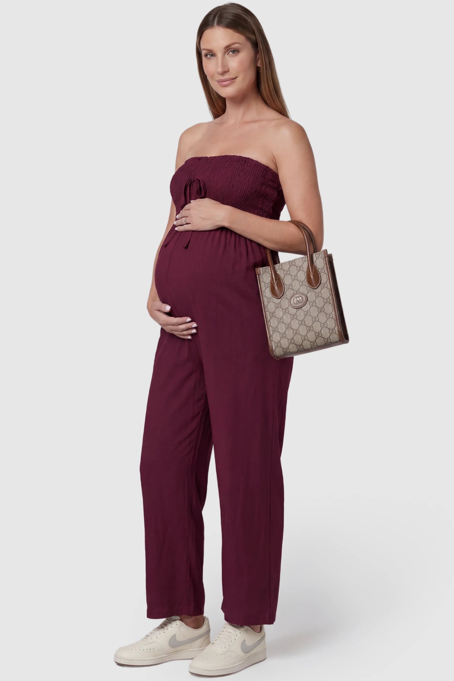 Strapless Smocked Bust Wide Leg Maternity Jumpsuit Strapless Smocked Bust Wide Leg Maternity Jumpsuit in Wine Red featuring a relaxed leg design on a pregnant model, side view.