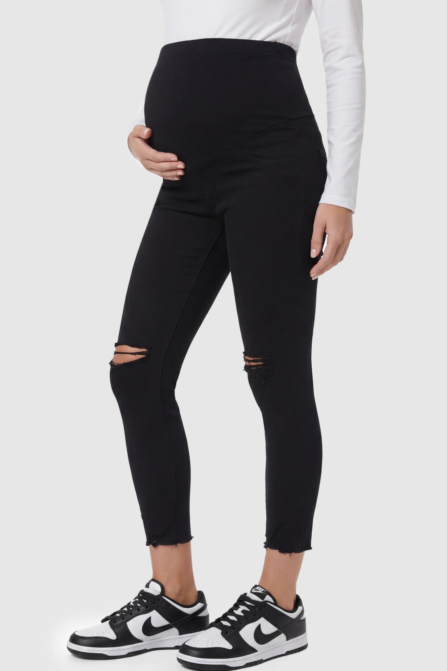 Stretch Panel Distressed Skinny Maternity Jeans Stretch Panel Distressed Skinny Maternity Jeans in Black featuring a high-rise elastic waistband and ripped knees on a pregnant model side view.
