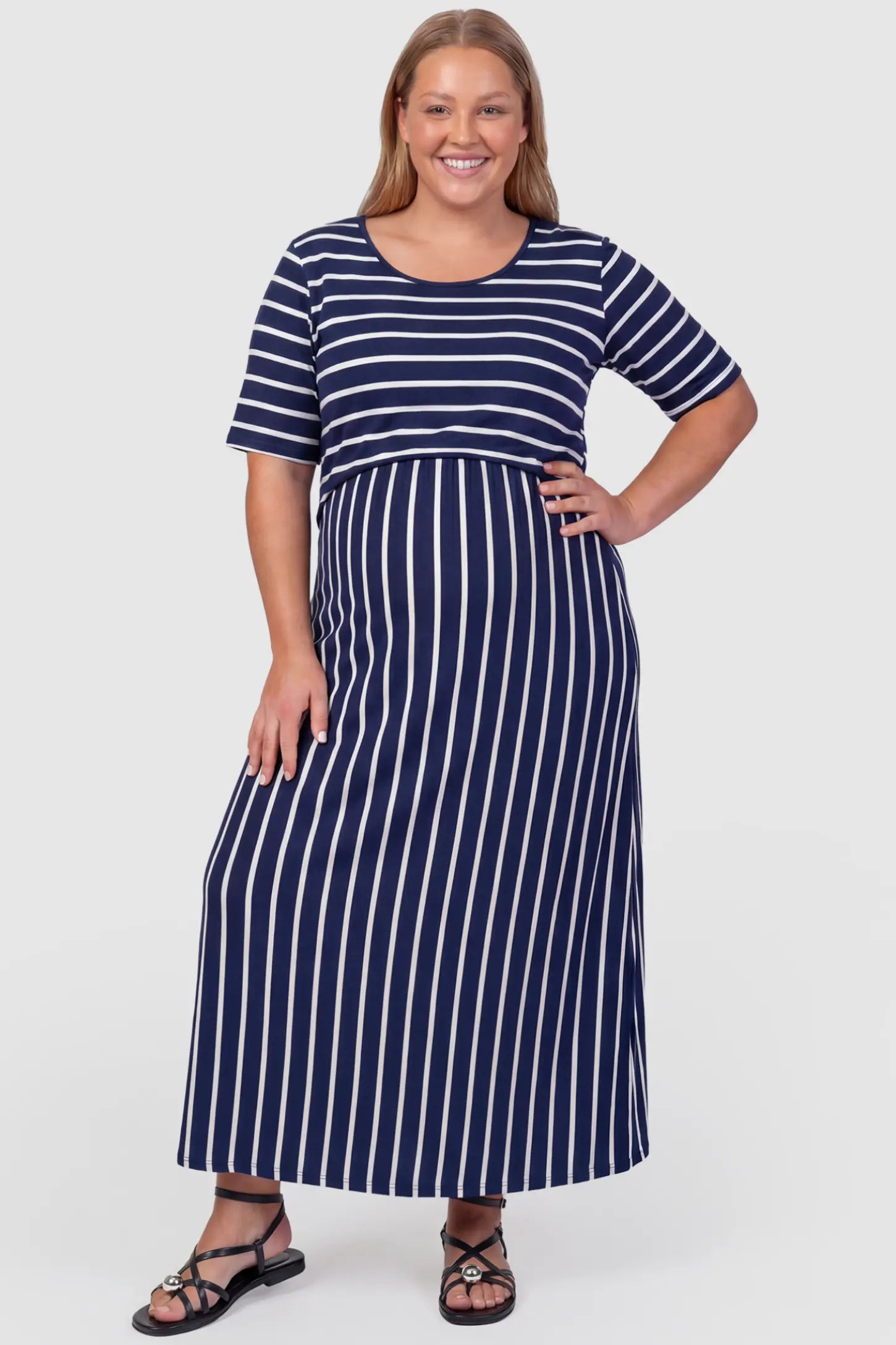 Striped Long Sleeve Maternity Maxi Dress Stretch Jersey Mixed-Stripe Maternity Maxi Dress in dark blue and White featuring an empire waist on a plus size pregnant model, front view.