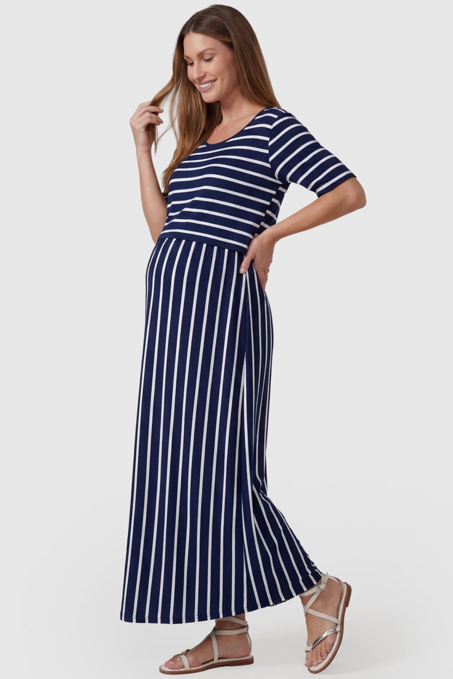 Striped Long Sleeve Maternity Maxi Dress Stretch Jersey Mixed-Stripe Maternity Maxi Dress in dark blue and White featuring an empire waist on a pregnant model, side view.