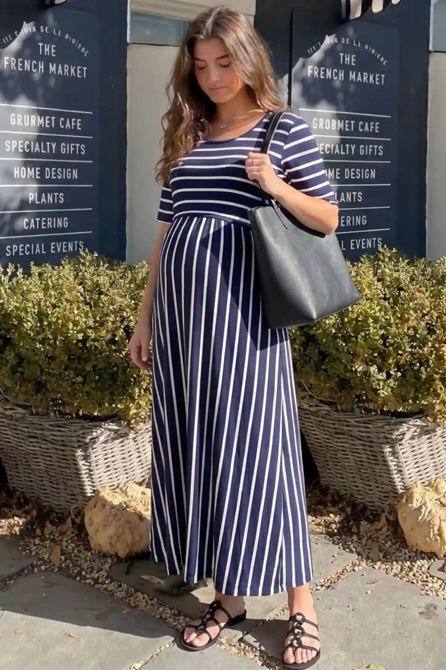 Striped Long Sleeve Maternity Maxi Dress Stretch Jersey Mixed-Stripe Maternity Maxi Dress in dark blue and White featuring an empire waist on a pregnant woman in an outdoor setting, side view.