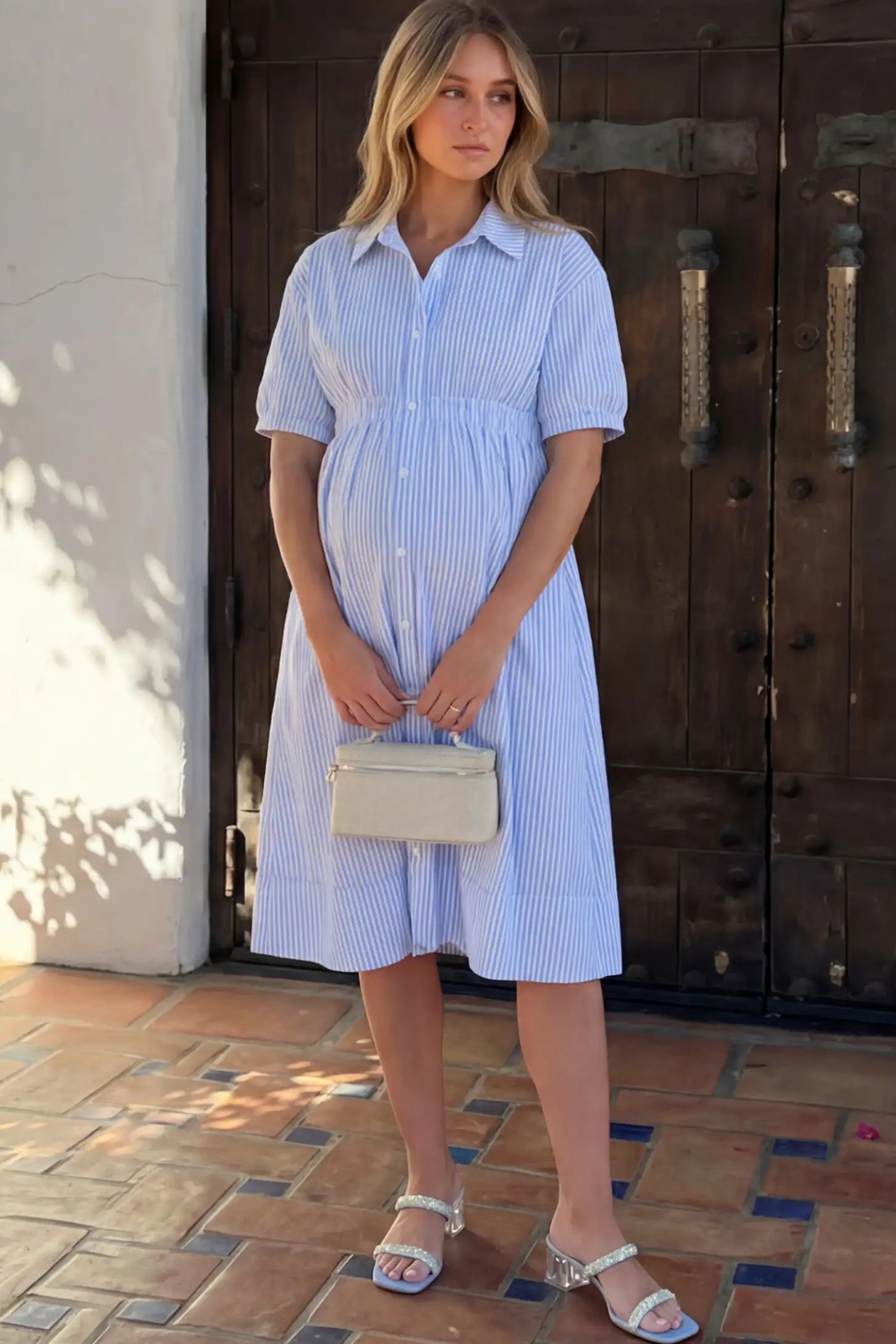 Striped Smocked-Waist Button-Down Maternity Shirt Dress in light blue and white stripes featuring a collared neckline and short sleeves on a pregnant woman.