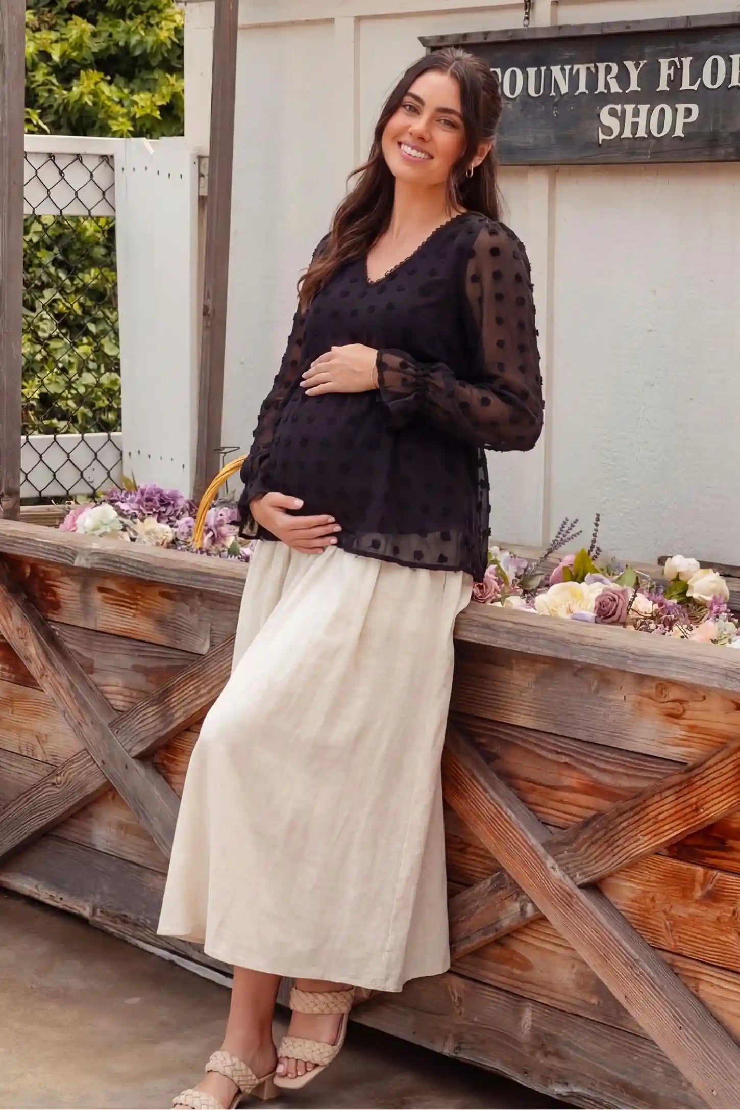Swiss Dot Sheer Empire Waist Maternity Top Swiss Dot Sheer Empire Waist Maternity Top in black featuring soft sheer material, editorial lifestyle view on a pregnant model outdoors.