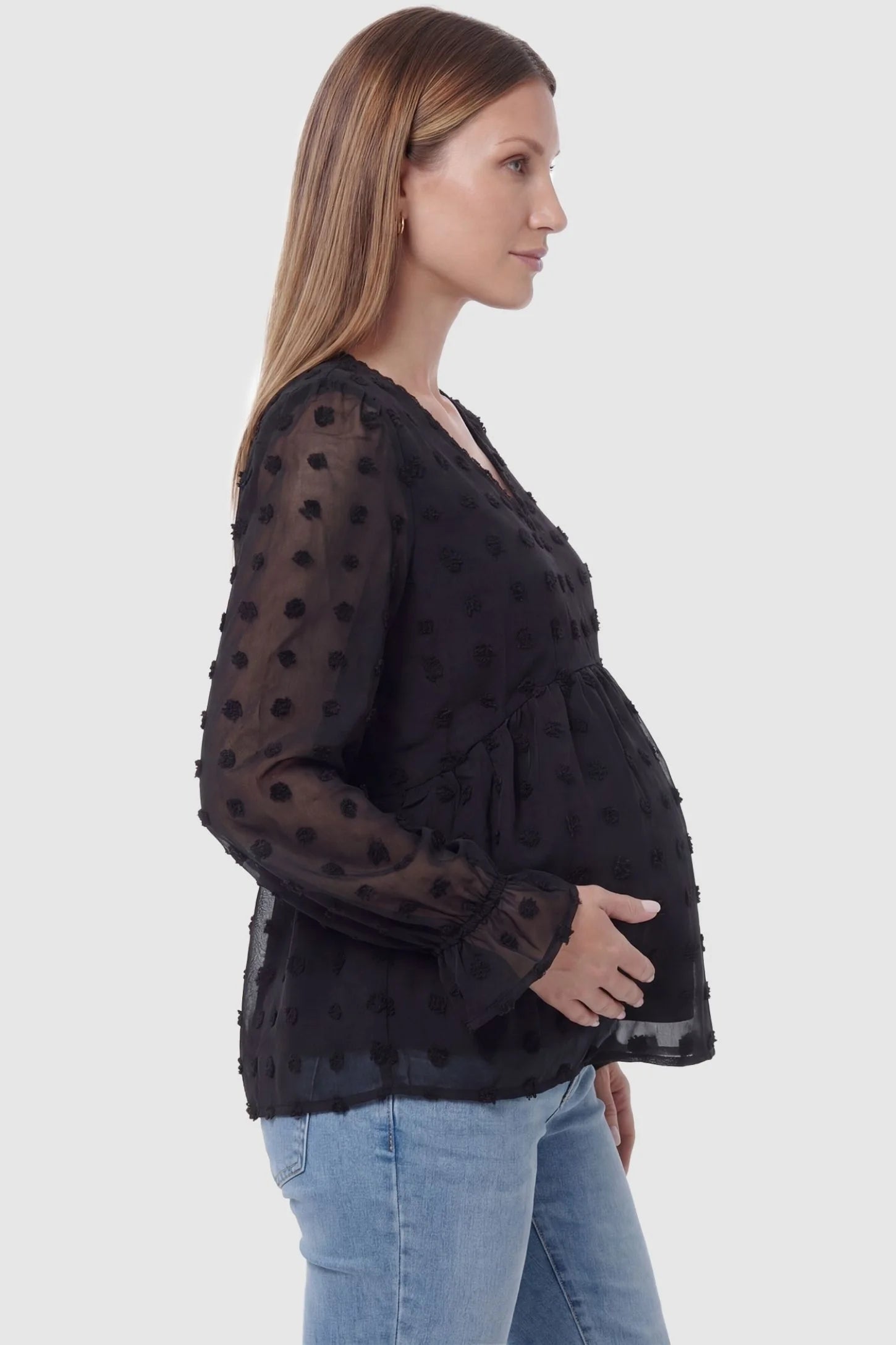 Swiss Dot Sheer Empire Waist Maternity Top in black featuring sheer polka dot sleeves, side view on a pregnant model.