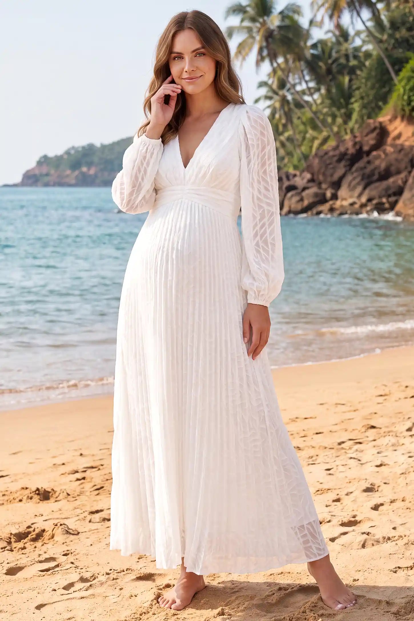 Textured Empire Waist Long Sleeve Maternity Maxi Dress in White featuring a pleated skirt shown on a pregnant woman cradling her bump at a garden party next to an outdoor bar, front view.