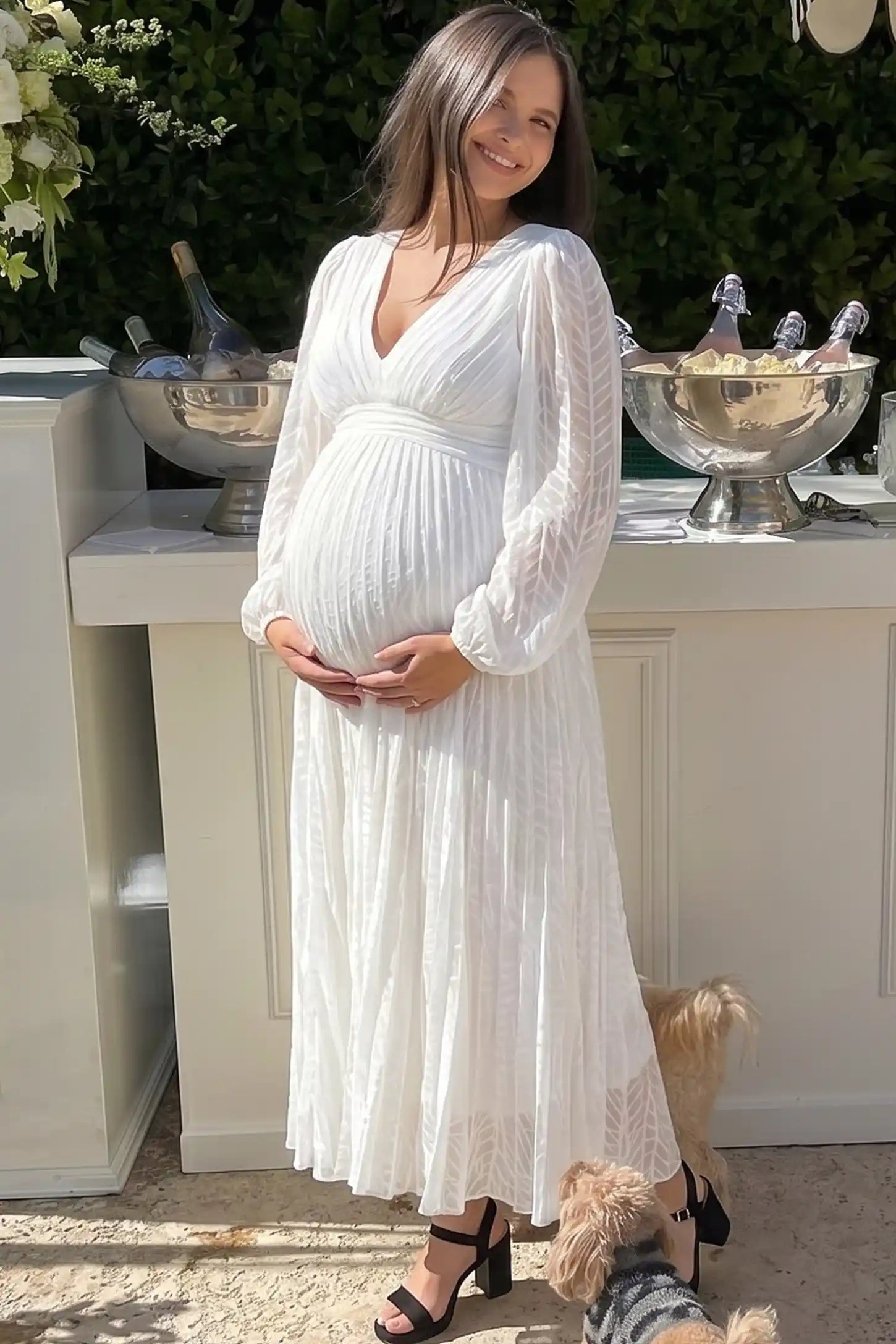 Textured Empire Waist Long Sleeve Maternity Maxi Dress in White featuring a pleated skirt on a pregnant woman in outdoor setting front view.