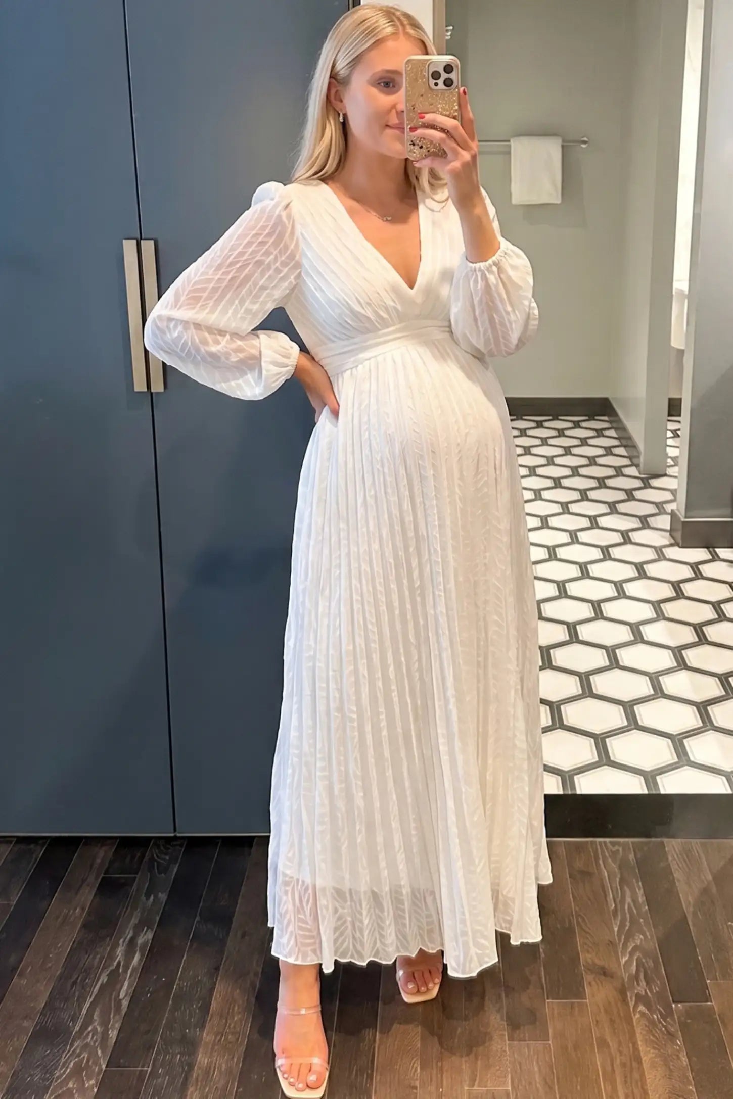 Textured Empire Waist Long Sleeve Maternity Maxi Dress Textured Empire Waist Long Sleeve Maternity Maxi Dress in White featuring a pleated skirt on a pregnant woman in indoor setting front view.