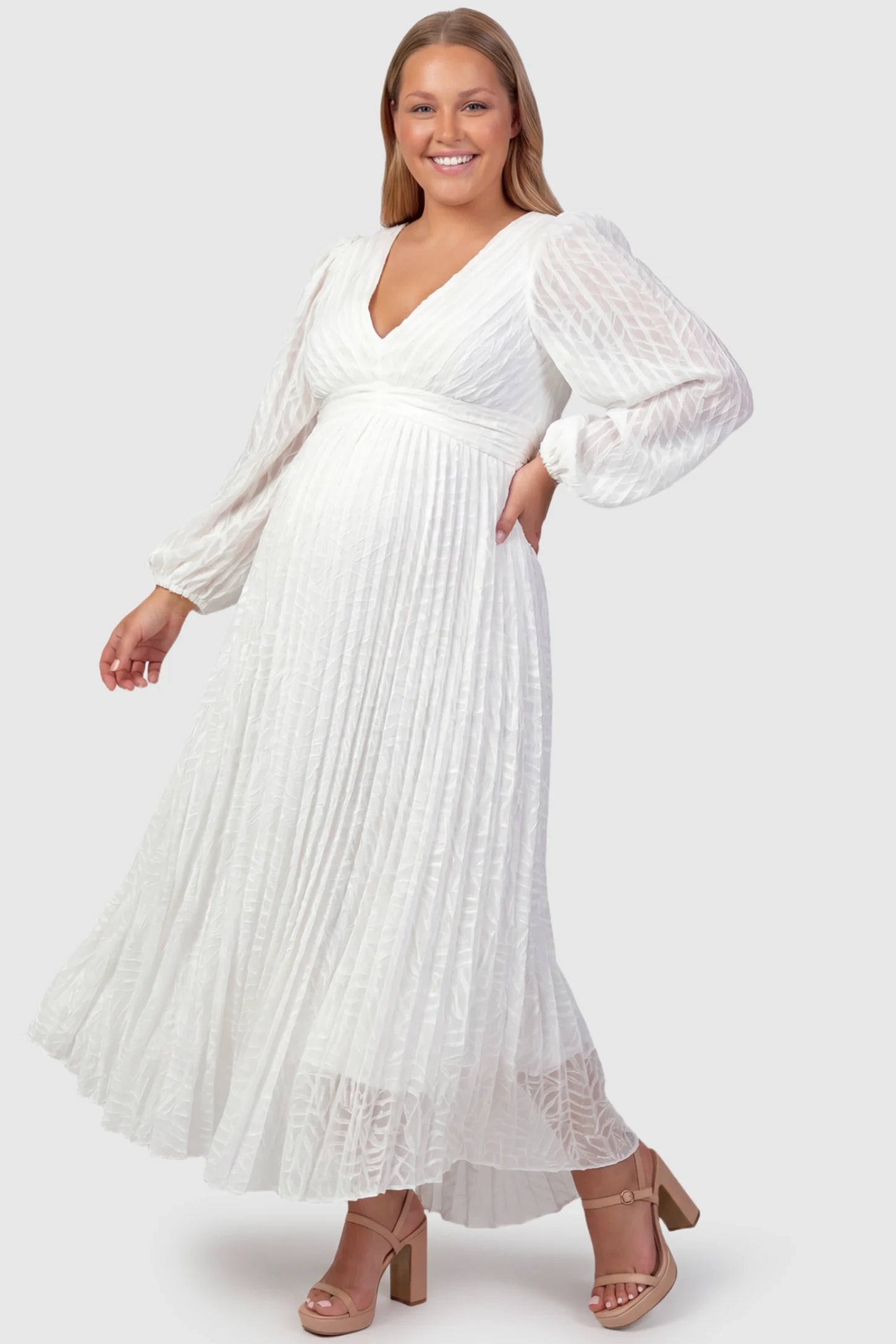 Textured Empire Waist Long Sleeve Maternity Maxi Dress Textured Empire Waist Long Sleeve Maternity Maxi Dress in White featuring a V-neck and pleated skirt on a plus size pregnant model front view.