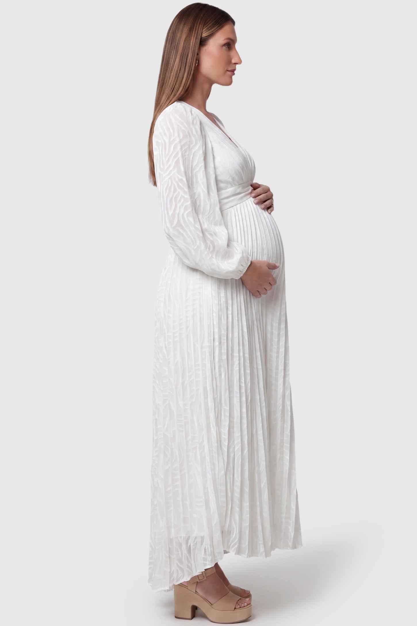 Textured Empire Waist Long Sleeve Maternity Maxi Dress Textured Empire Waist Long Sleeve Maternity Maxi Dress in White featuring a V-neck and pleated skirt on a pregnant model side view.