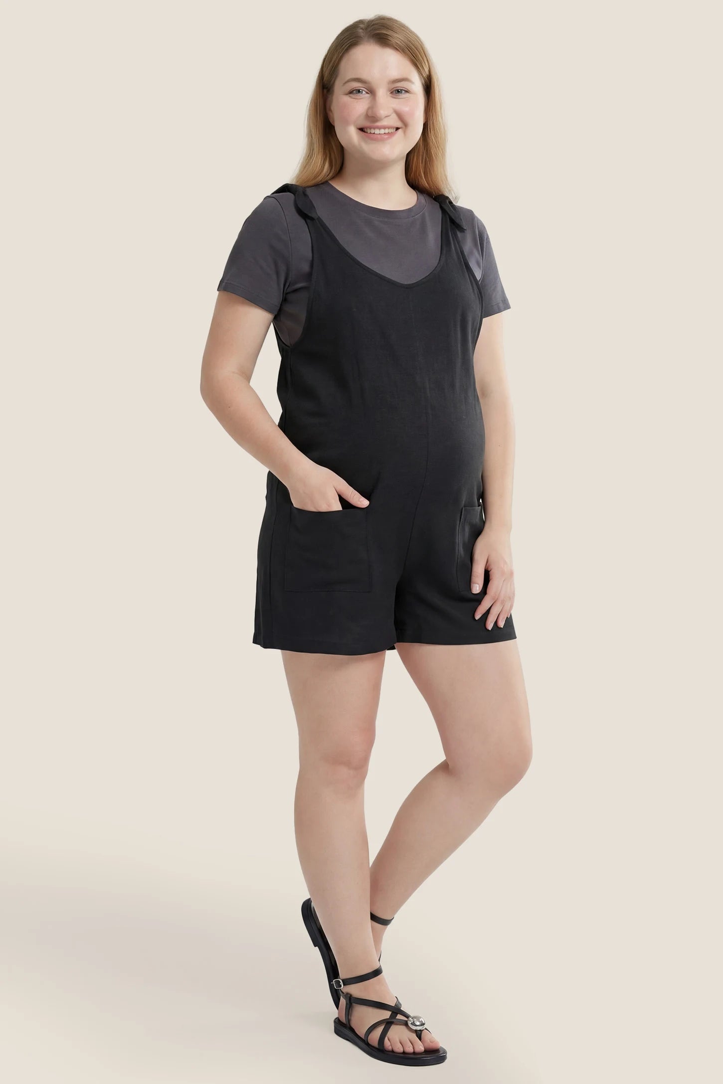 Full body view of the black Tie-Strap Sleeveless Pocketed Maternity Romper styled for casual everyday maternity wear.