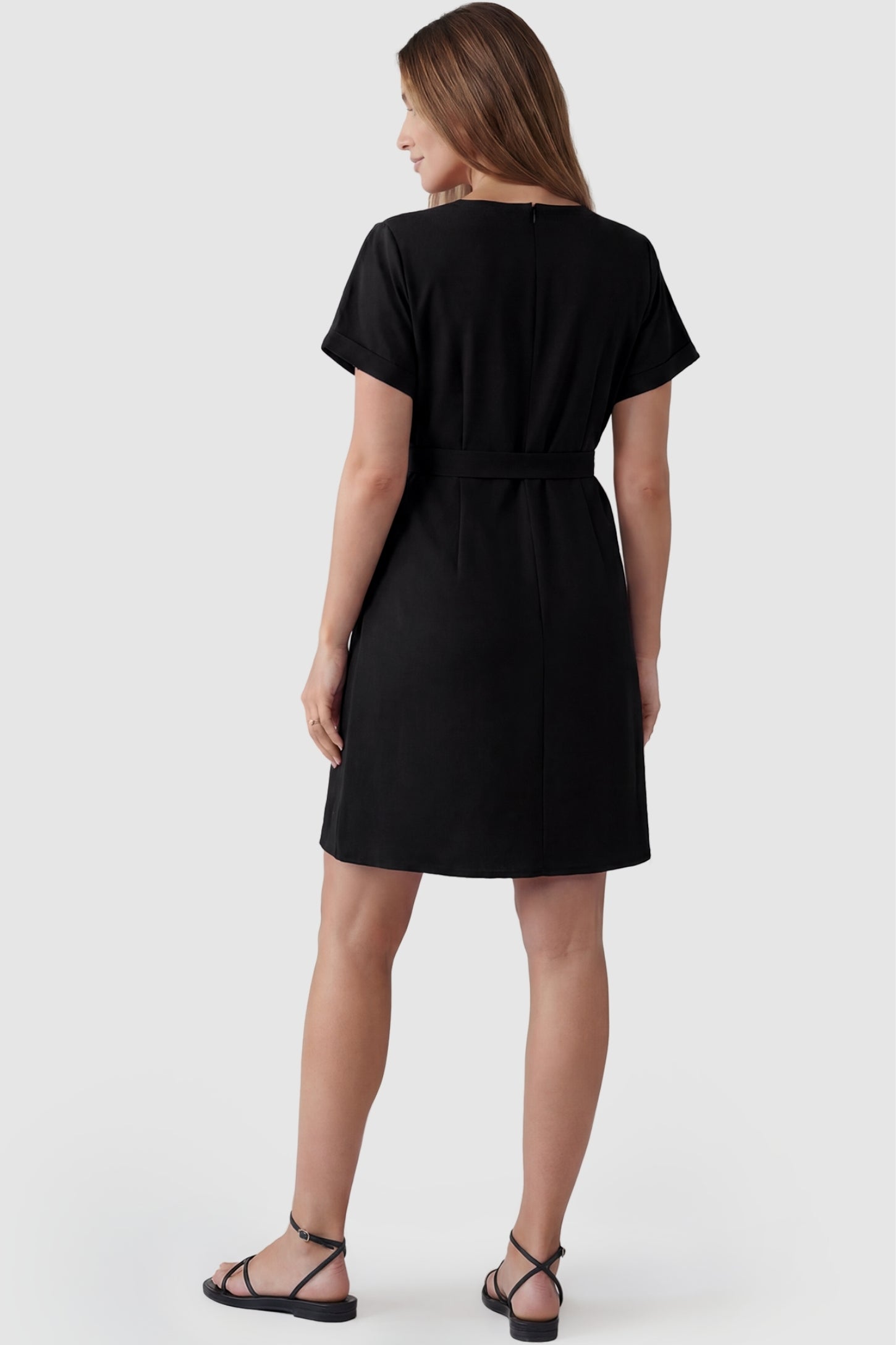 Lightweight Short Sleeve Tie Waist Flowy Maternity Mini Dress Lightweight Short Sleeve Tie Waist Flowy Maternity Mini Dress in Black featuring a concealed back zip and cuffed short sleeves on a pregnant model, back view.