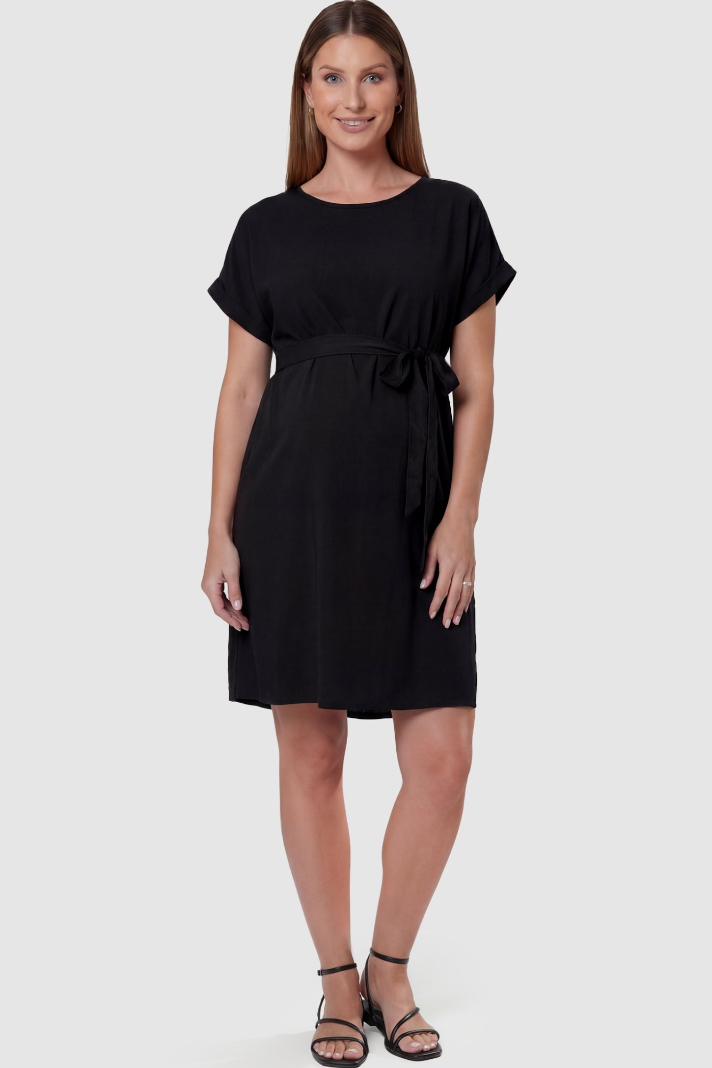 Lightweight Short Sleeve Tie Waist Flowy Maternity Mini Dress Lightweight Short Sleeve Tie Waist Flowy Maternity Mini Dress in Black featuring a relaxed empire waist tie on a pregnant model, front view.