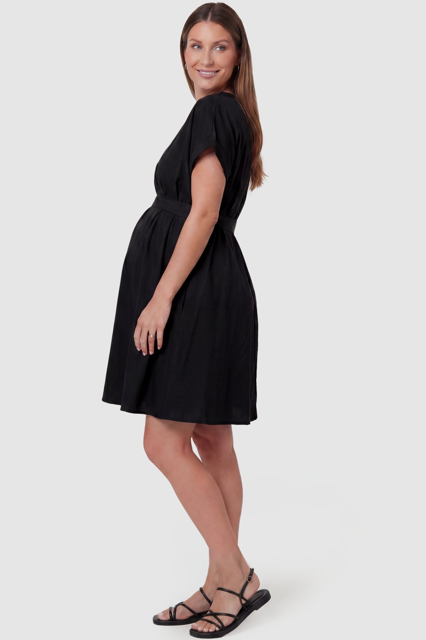 Lightweight Short Sleeve Tie Waist Flowy Maternity Mini Dress Lightweight Short Sleeve Tie Waist Flowy Maternity Mini Dress in Black featuring a flowy gathered skirt on a pregnant model, side view.