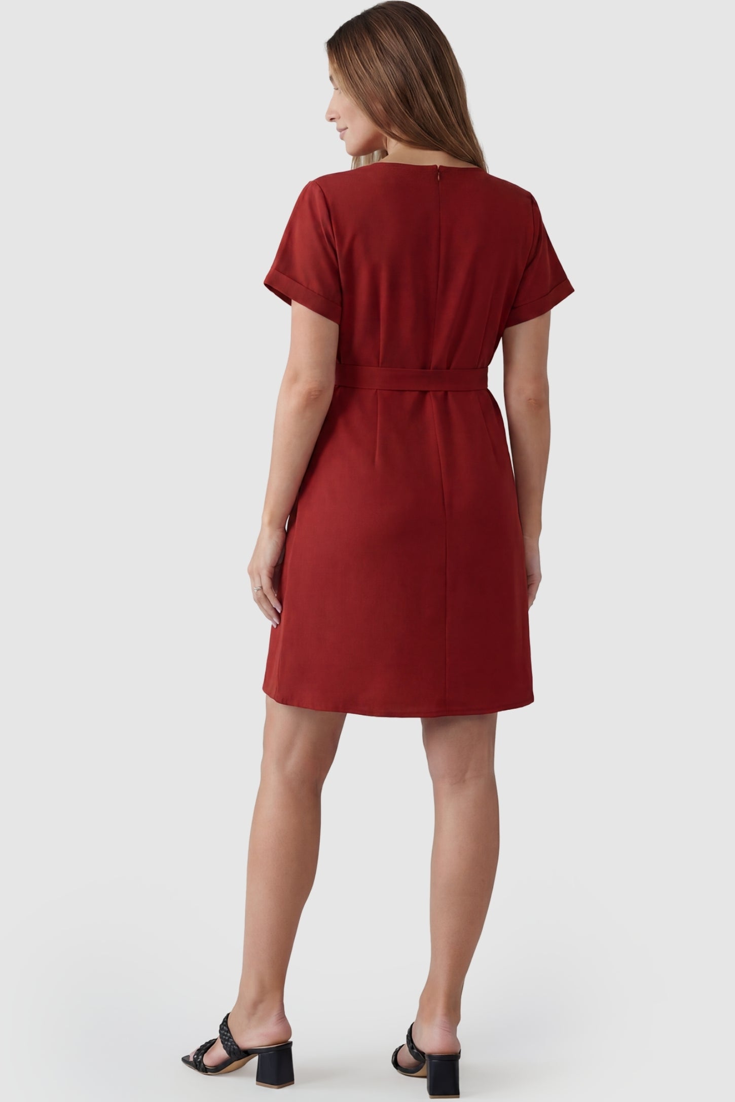 Lightweight Short Sleeve Tie Waist Flowy Maternity Mini Dress Lightweight Short Sleeve Tie Waist Flowy Maternity Mini Dress in Rust featuring a concealed back zip and cuffed short sleeves on a pregnant model, back view.