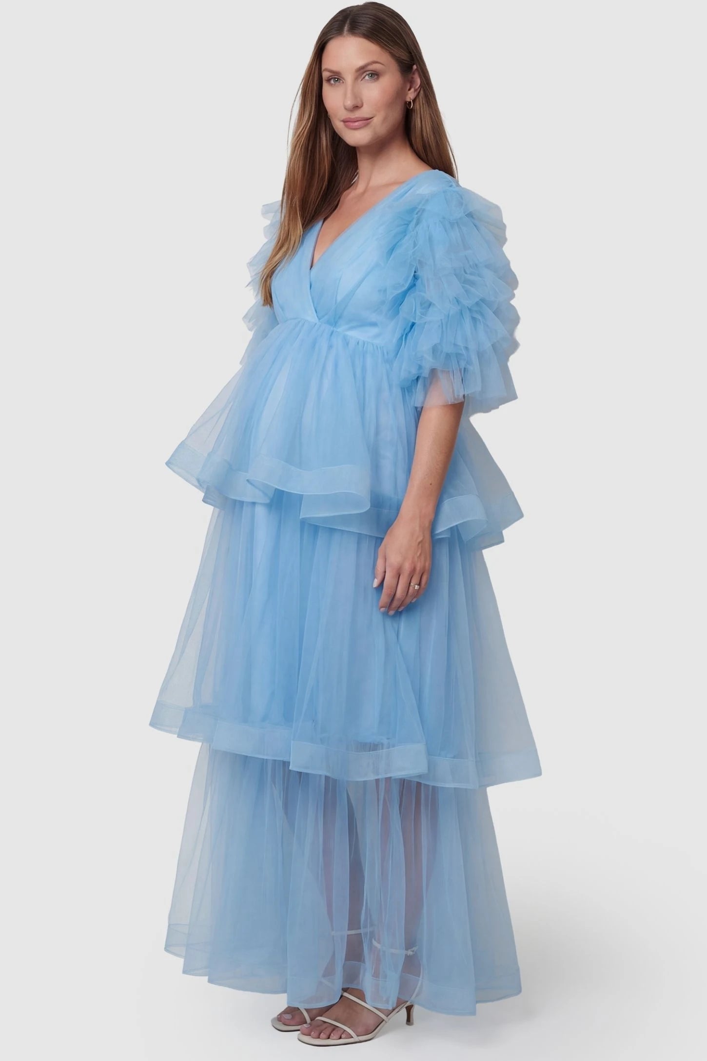 Tiered Ruffled Tulle Flutter Sleeve Maternity Maxi Gown Tiered Ruffled Tulle Flutter Sleeve Maternity Maxi Gown in Blue with a soft v-neckline and tiered layers on pregnant model, side view.
