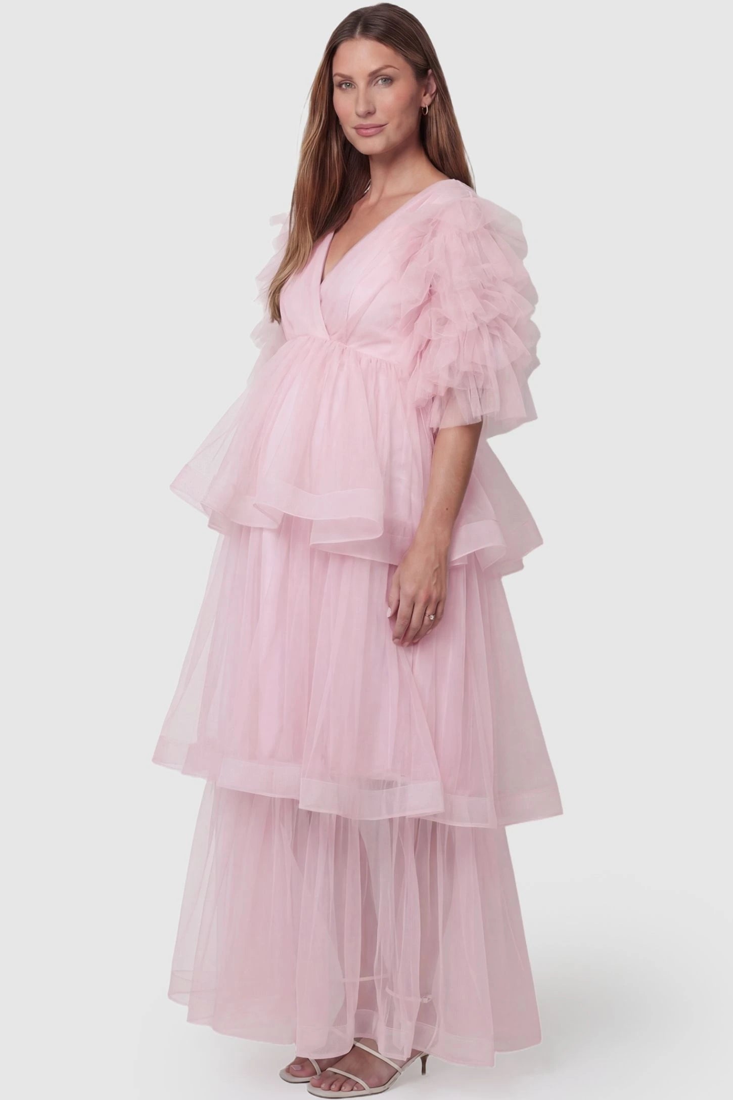 Tiered Ruffled Tulle Flutter Sleeve Maternity Maxi Gown Tiered Ruffled Tulle Flutter Sleeve Maternity Maxi Gown in Pink with a soft v-neckline and tiered layers on pregnant model, side view.