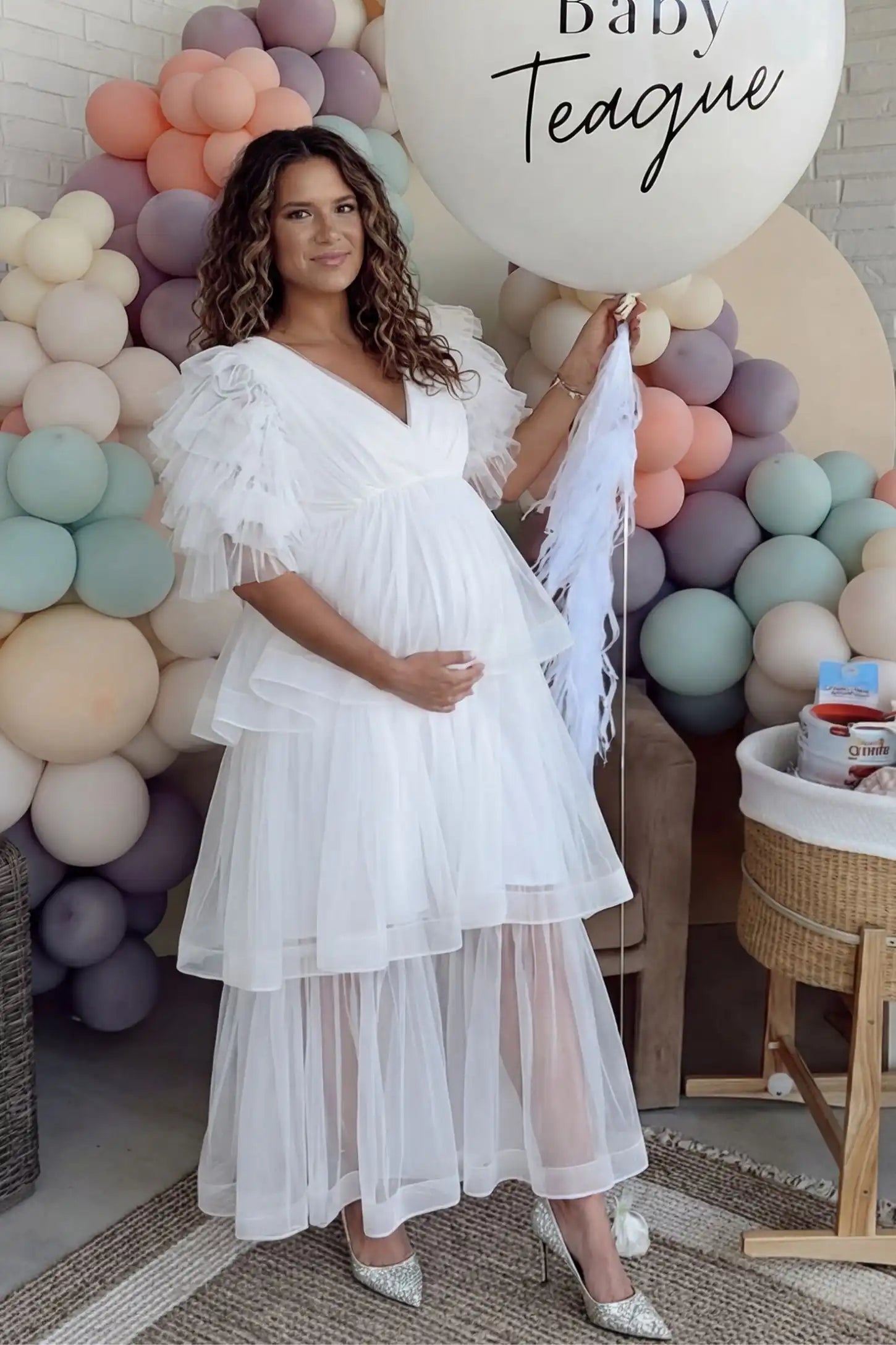 Tiered Ruffled Tulle Flutter Sleeve Maternity Maxi Gown Tiered Ruffled Tulle Flutter Sleeve Maternity Maxi Gown in White with statement flutter sleeves on pregnant model at baby shower, front view.