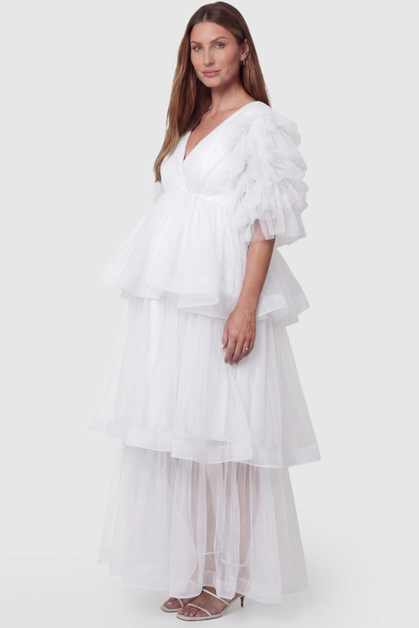 Tiered Ruffled Tulle Flutter Sleeve Maternity Maxi Gown Tiered Ruffled Tulle Flutter Sleeve Maternity Maxi Gown in White with a soft v-neckline and tiered layers on pregnant model, side view.