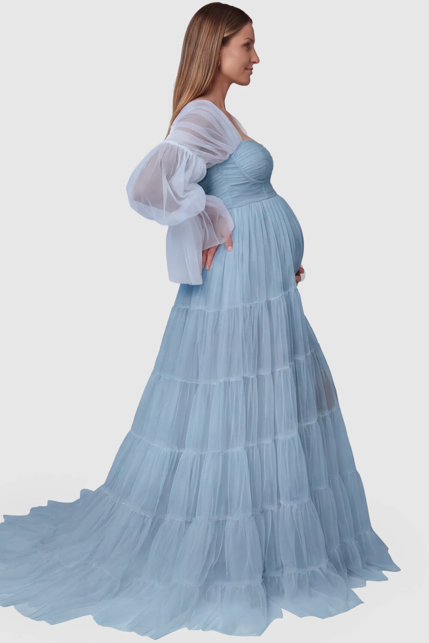 Tiered Tulle Long Sleeve Maternity Photoshoot Gown Tiered Tulle Long Sleeve Maternity photoshoot Gown in Blue featuring a sweetheart neckline and voluminous tulle layers on a pregnant model, side view.