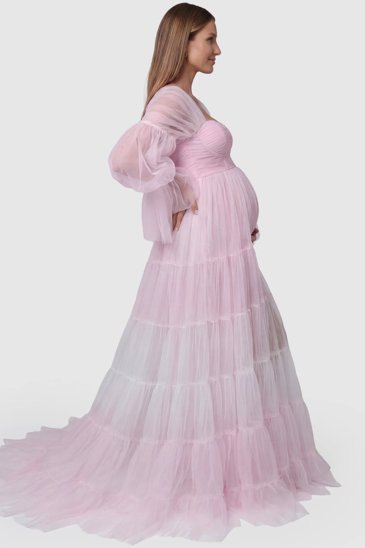 Tiered Tulle Long Sleeve Maternity Photoshoot Gown Tiered Tulle Long Sleeve Maternity photoshoot Gown in Pink featuring a sweetheart neckline and voluminous tulle layers on a pregnant model, side view.