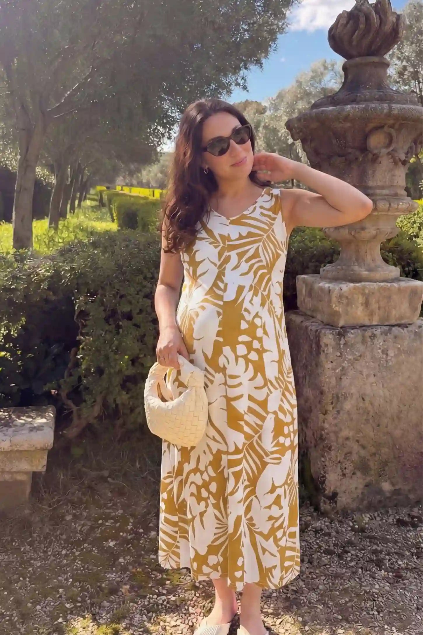 Tropical Print Sleeveless Midi Maternity Dress Tropical Print V-Back Sleeveless Midi Maternity Dress in Orange featuring a vibrant tropical pattern on a model in a garden setting, front view.