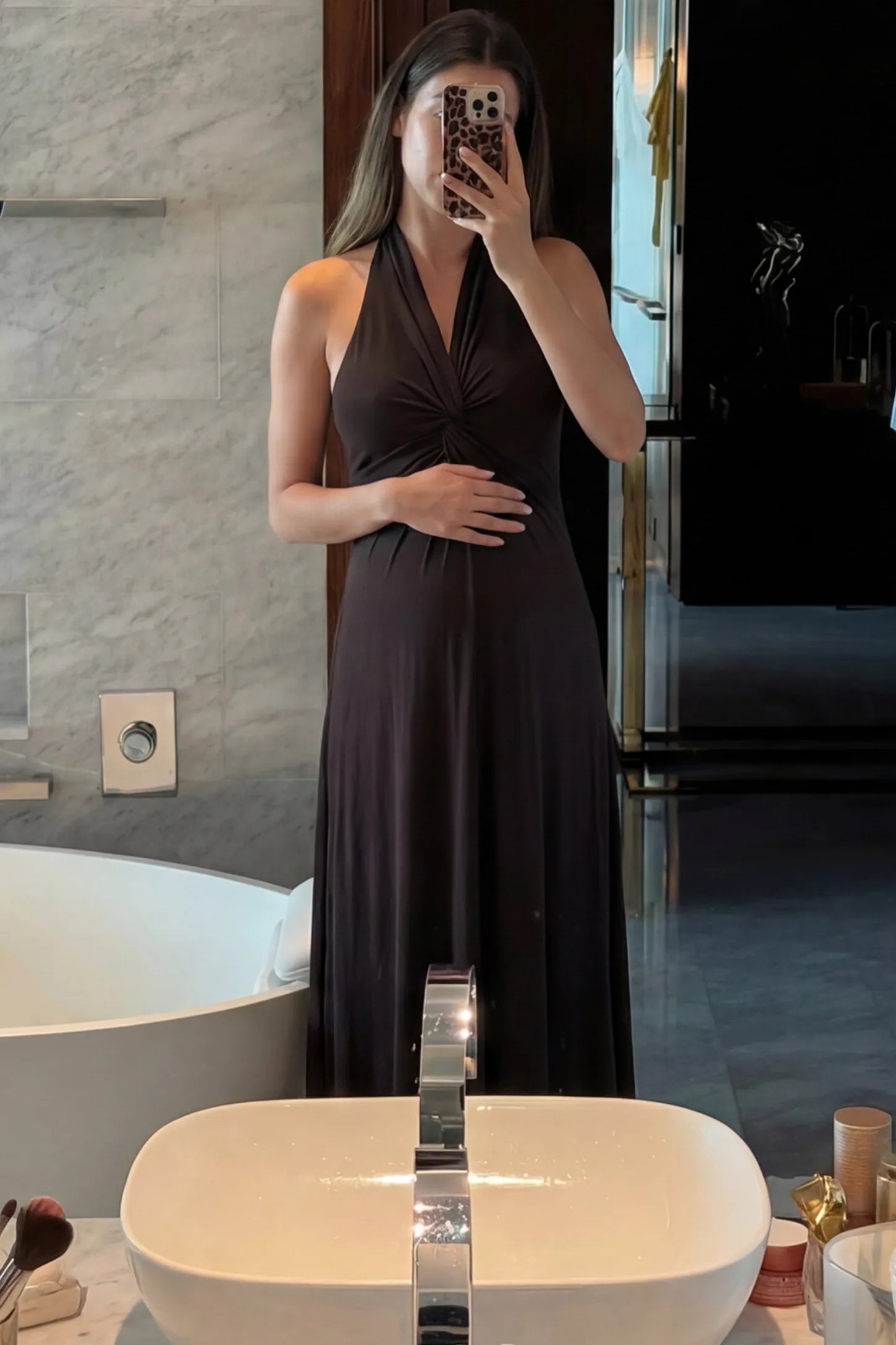 Twist Front Halter Neck Maternity Maxi Dress Twist Front Halter Neck Maternity Maxi Dress in Black featuring knot detail, sleeveless, A-line silhouette on a pregnant woman, front view.