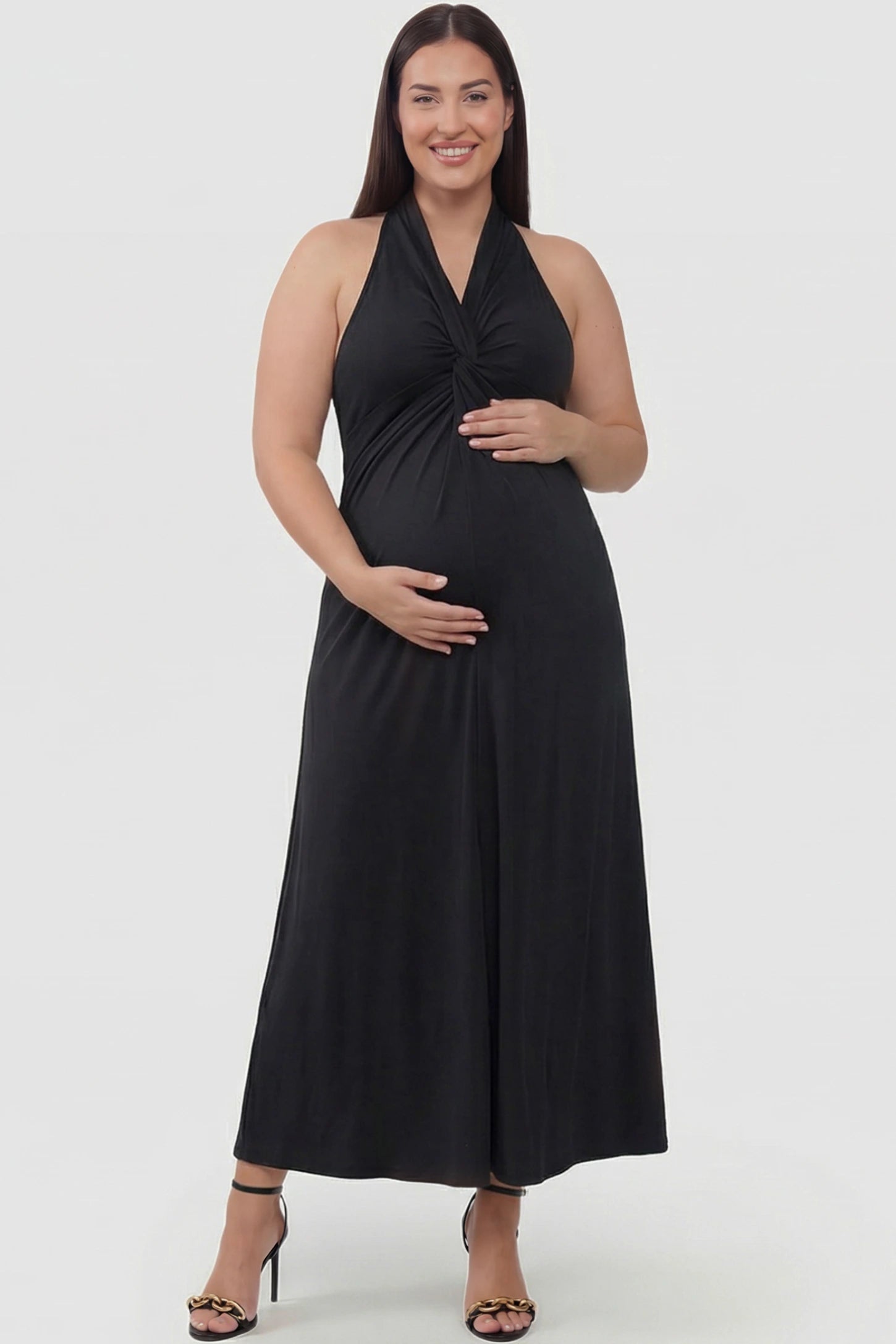Twist Front Halter Neck Maternity Maxi Dress Twist Front Halter Neck Maternity Maxi Dress in Black featuring knot detail, sleeveless, A-line silhouette on a plus size pregnant model, front view.