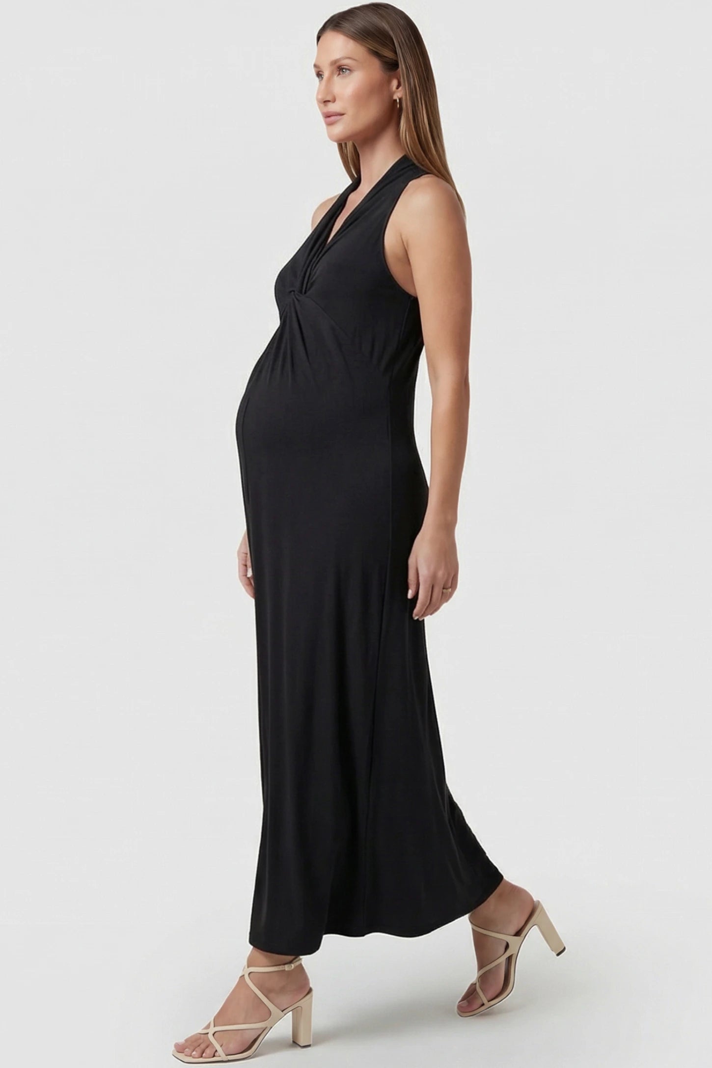 Twist Front Halter Neck Maternity Maxi Dress Twist Front Halter Neck Maternity Maxi Dress in Black featuring knot detail, sleeveless, A-line silhouette on a pregnant model, side view.