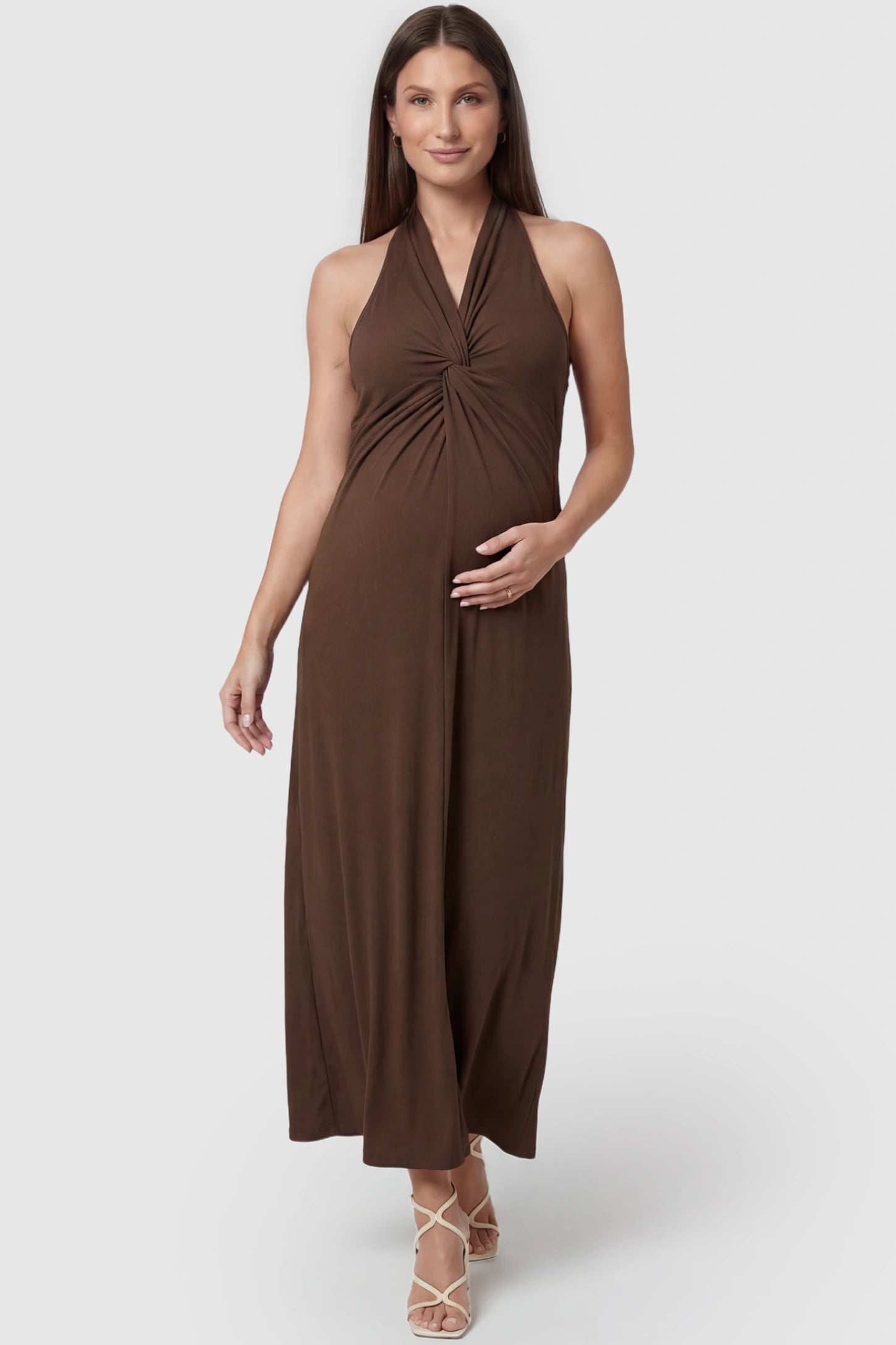 Twist Front Halter Neck Maternity Maxi Dress Twist Front Halter Neck Maternity Maxi Dress in Coffee featuring knot detail, sleeveless, A-line silhouette on a pregnant model, front view.