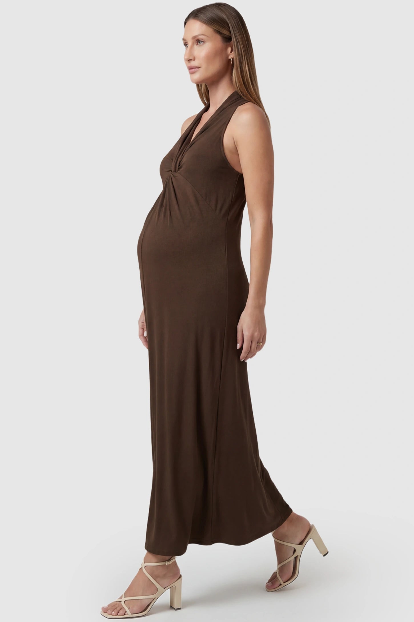 Twist Front Halter Neck Maternity Maxi Dress Twist Front Halter Neck Maternity Maxi Dress in Coffee featuring knot detail, sleeveless, A-line silhouette on a pregnant model, side view.