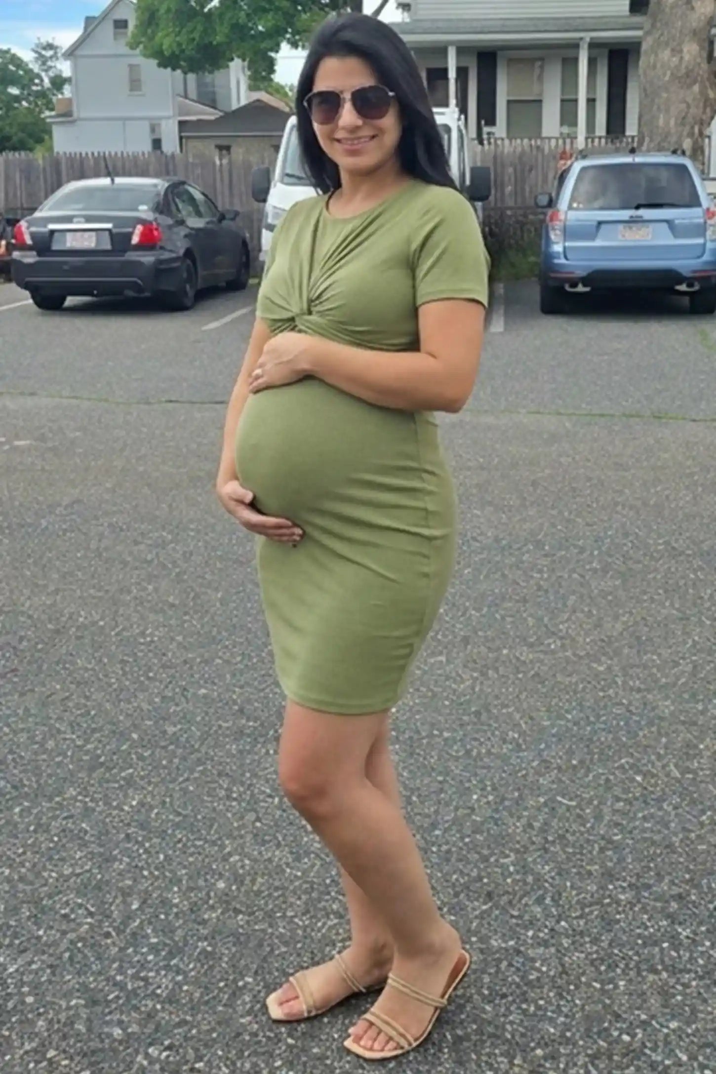 Twist Front Round Neck Short Sleeve Maternity Short Dress Twist Front Round Neck Maternity Short Dress in green featuring side ruched panels on a pregnant model in a parking lot, front view.