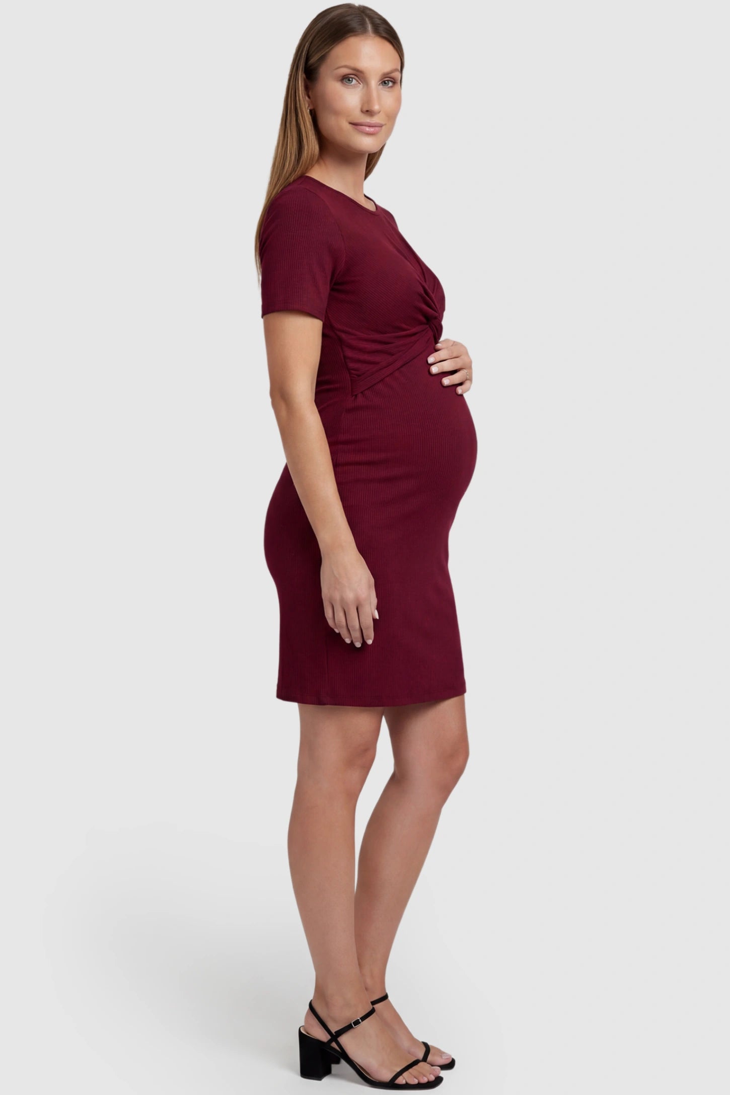 Twist Front Round Neck Short Sleeve Maternity Short Dress Twist Front Round Neck Maternity Short Dress in wine red featuring side ruched panels on a pregnant model, side view.