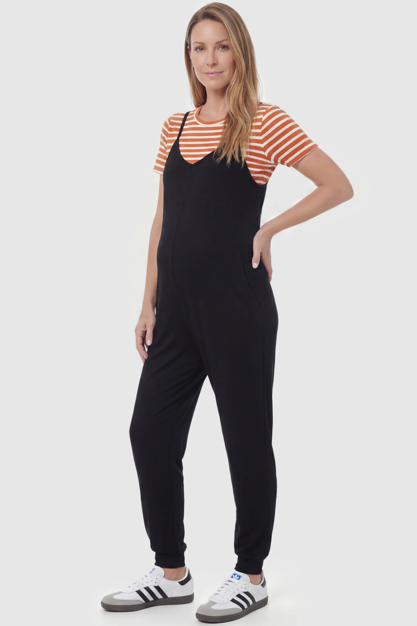V-Neck Pocketed Maternity Jogger Jumpsuit V-Neck Pocketed Maternity Jogger Jumpsuit in Black featuring cotton-spandex jersey and side pockets on a postpartum model, front view.