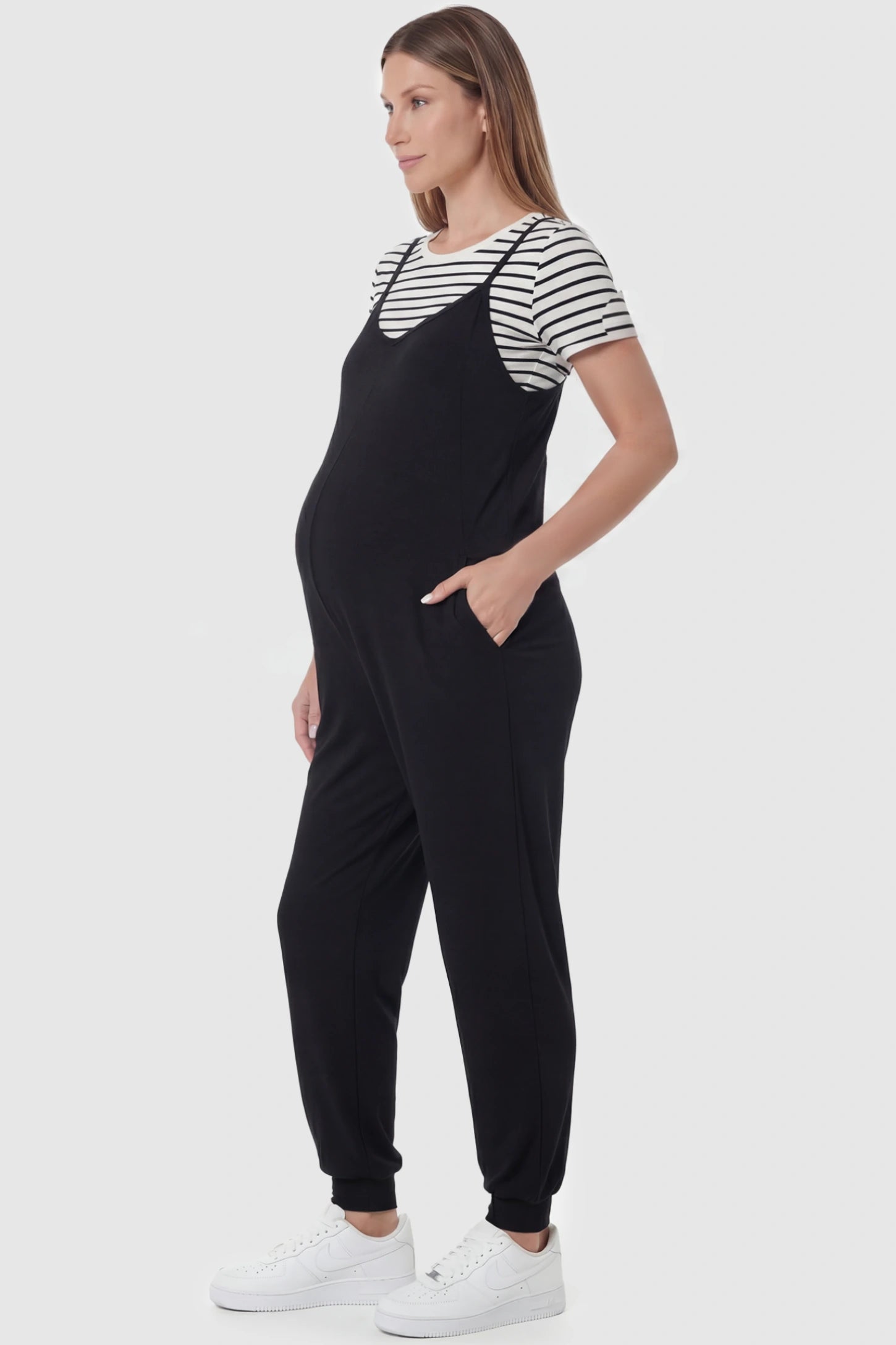 V-Neck Pocketed Maternity Jogger Jumpsuit V-Neck Pocketed Maternity Jogger Jumpsuit in Black featuring cotton-spandex jersey and side pockets on a pregnant model, side view.