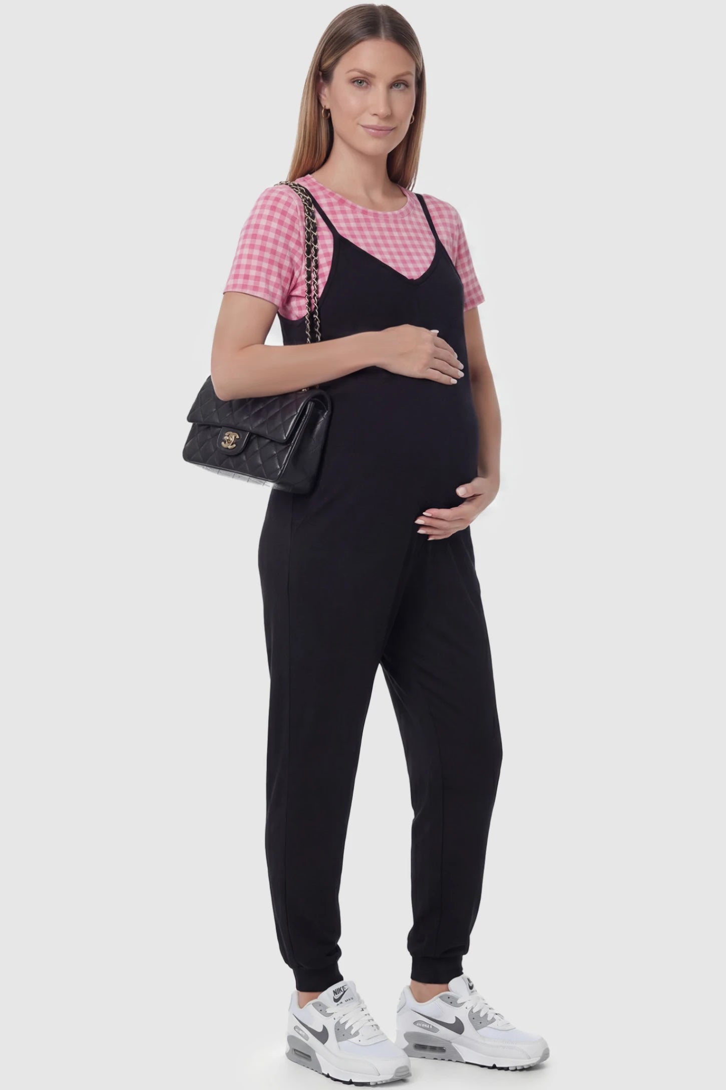 V-Neck Pocketed Maternity Jogger Jumpsuit in Black featuring cotton-spandex jersey and side pockets on a pregnant model, side view.