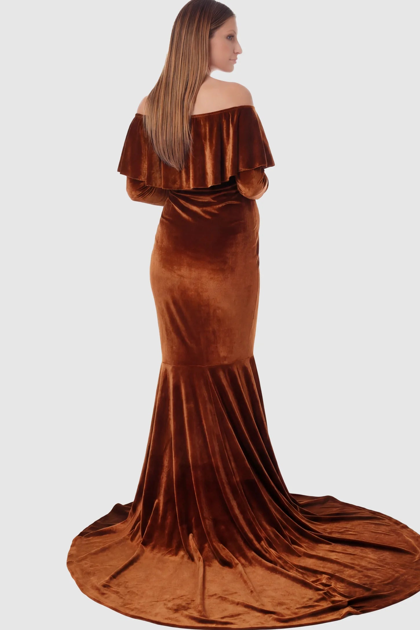 Velvet Off Shoulder Long Sleeve Maternity Mermaid Gown Velvet Off-the-Shoulder Maternity Mermaid Gown in Brown featuring a ruffled neckline and long sleeves on a pregnant model showing back.