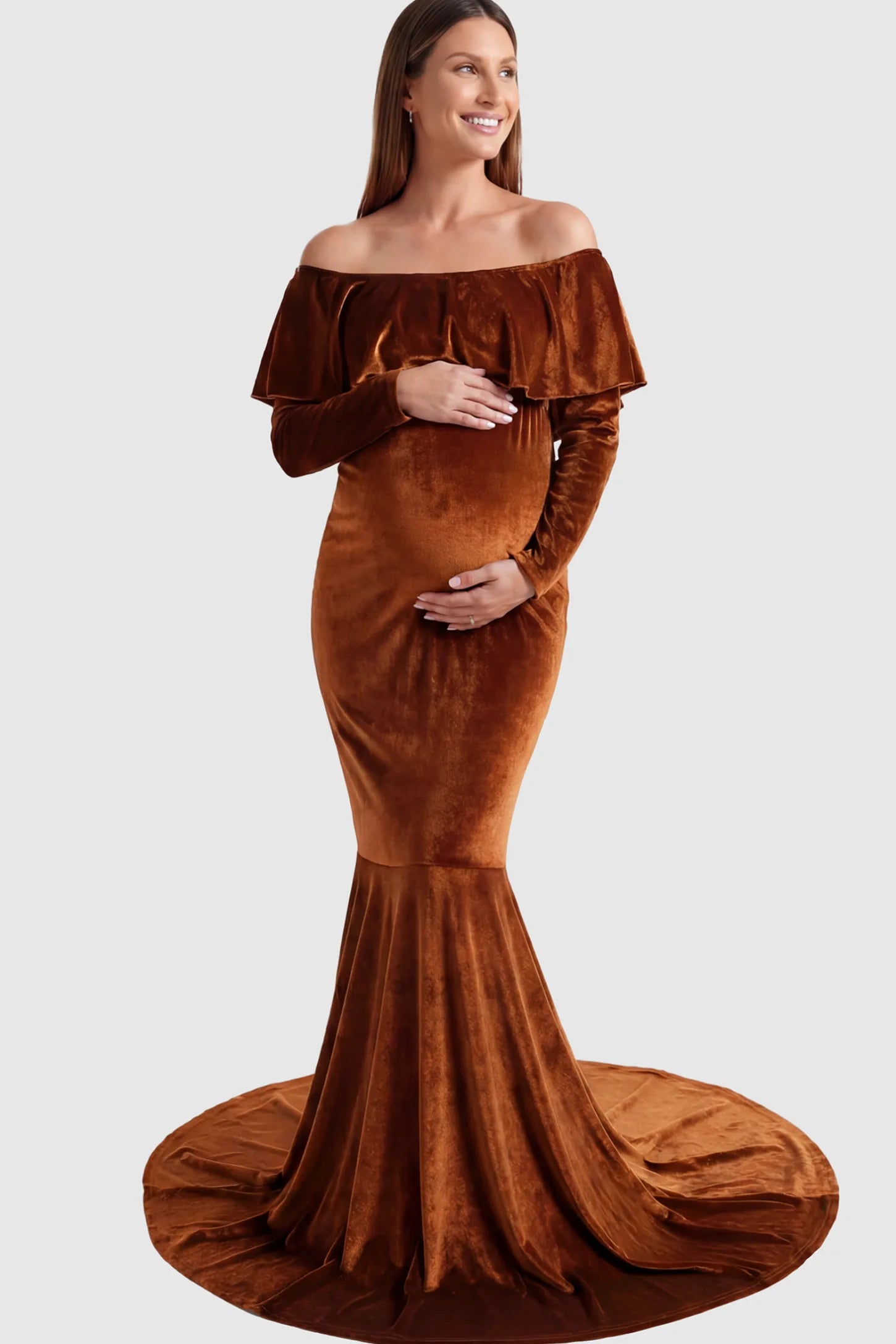 Velvet Off Shoulder Long Sleeve Maternity Mermaid Gown Velvet Off-the-Shoulder Maternity Mermaid Gown in Brown featuring a ruffled neckline and long sleeves on a pregnant model posing front.