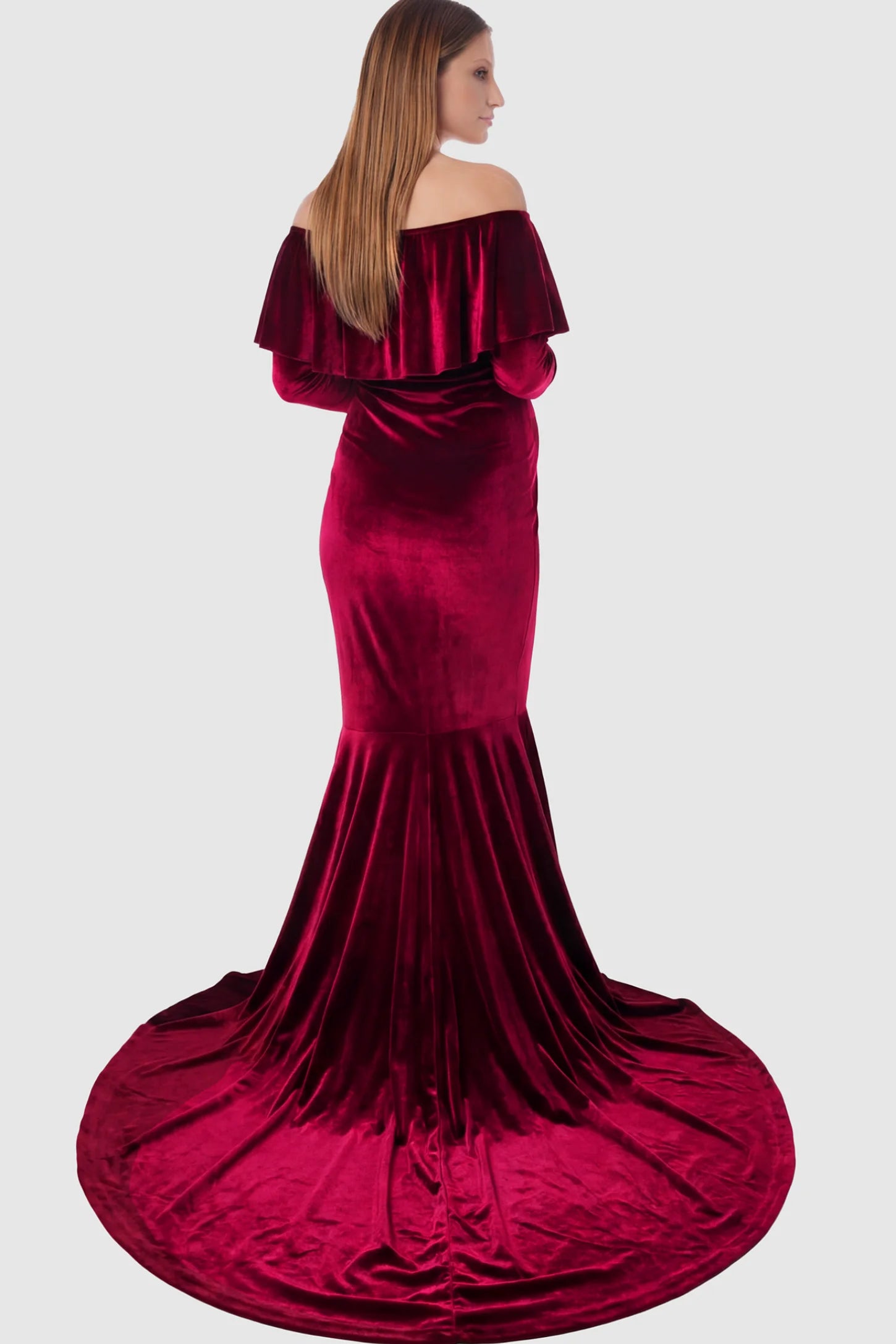 Velvet Off Shoulder Long Sleeve Maternity Mermaid Gown Velvet Off-the-Shoulder Maternity Mermaid Gown in Burgundy featuring a ruffled neckline and long sleeves on a pregnant model showing back.