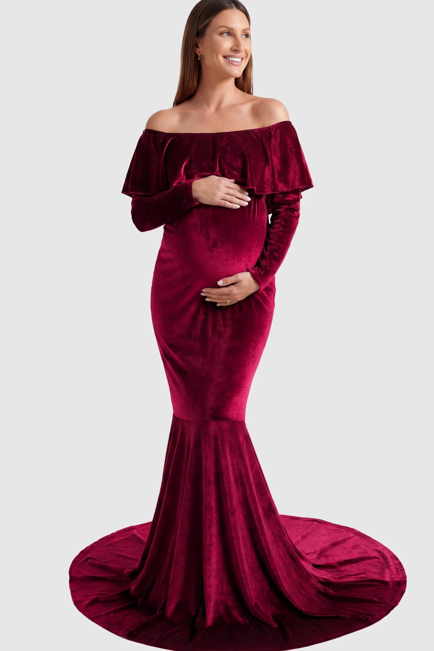 Velvet Off Shoulder Long Sleeve Maternity Mermaid Gown Velvet Off-the-Shoulder Maternity Mermaid Gown in Burgundy featuring a ruffled neckline and long sleeves on a pregnant model posing front.