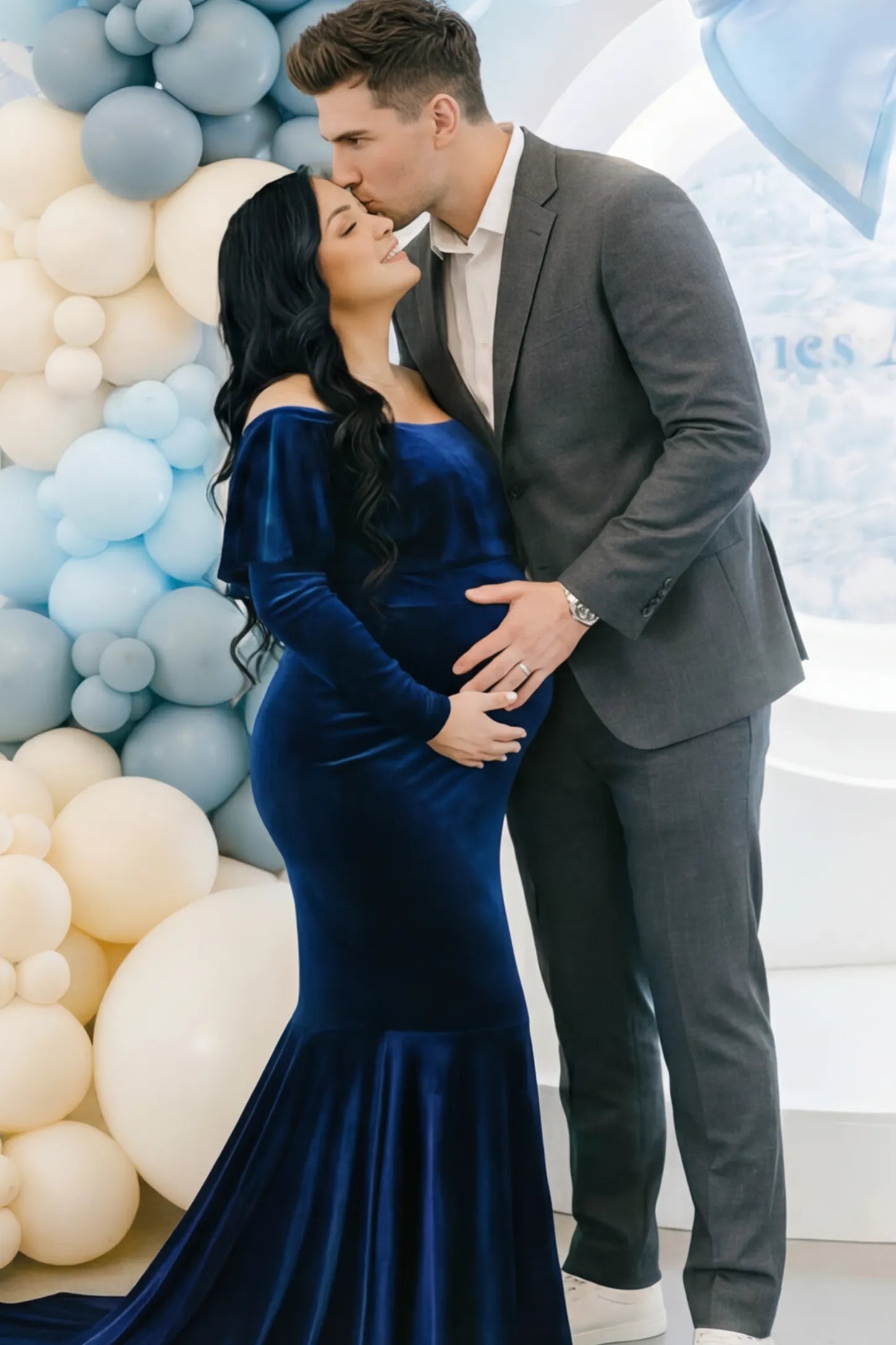 Velvet Off Shoulder Long Sleeve Maternity Mermaid Gown Velvet Off-the-Shoulder Maternity Mermaid Gown in Dark Blue featuring a ruffled neckline and long sleeves on a model posing with a partner.