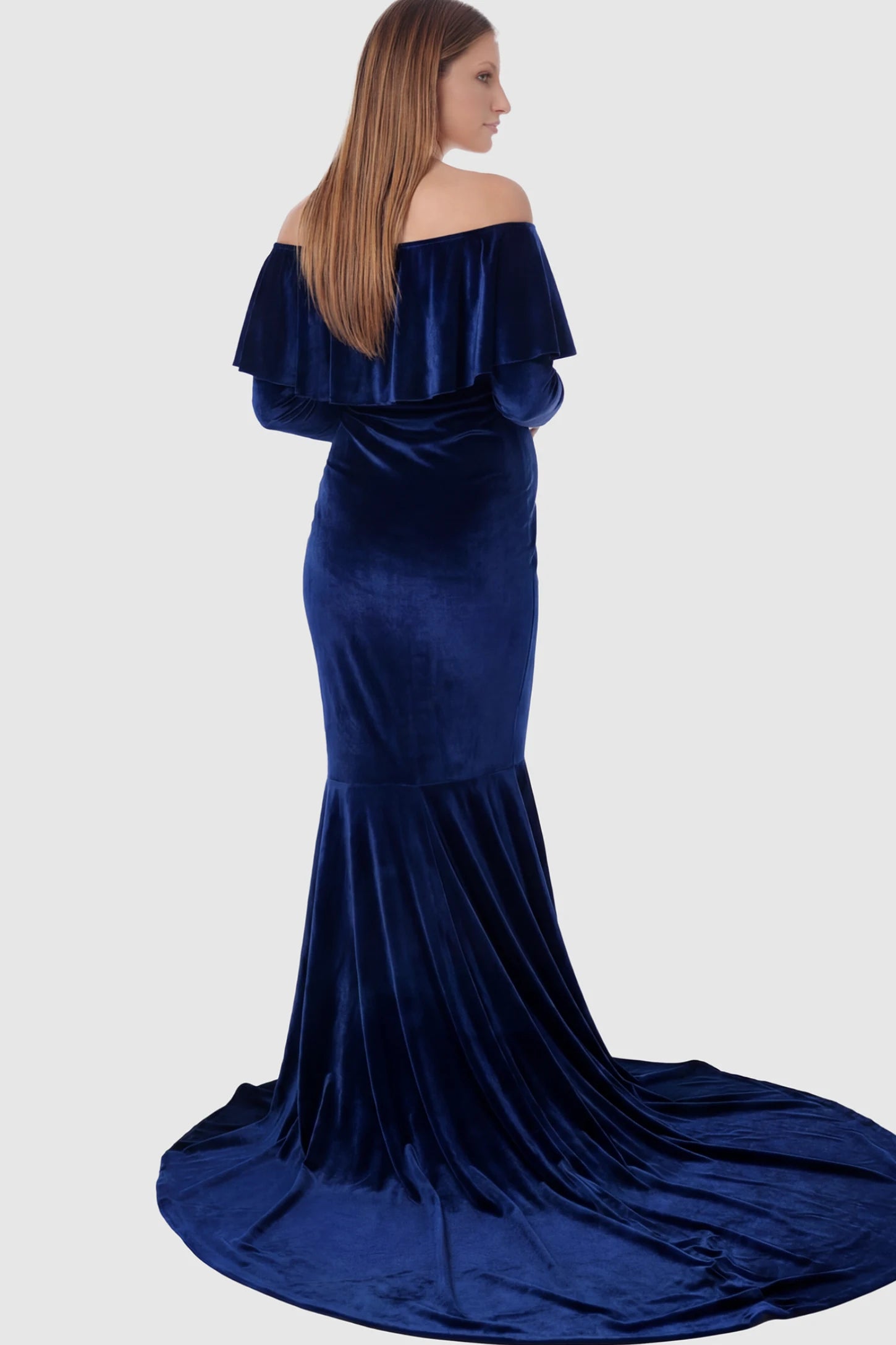 Velvet Off Shoulder Long Sleeve Maternity Mermaid Gown Velvet Off-the-Shoulder Maternity Mermaid Gown in Dark Blue featuring a ruffled neckline and long sleeves on a pregnant model showing back.