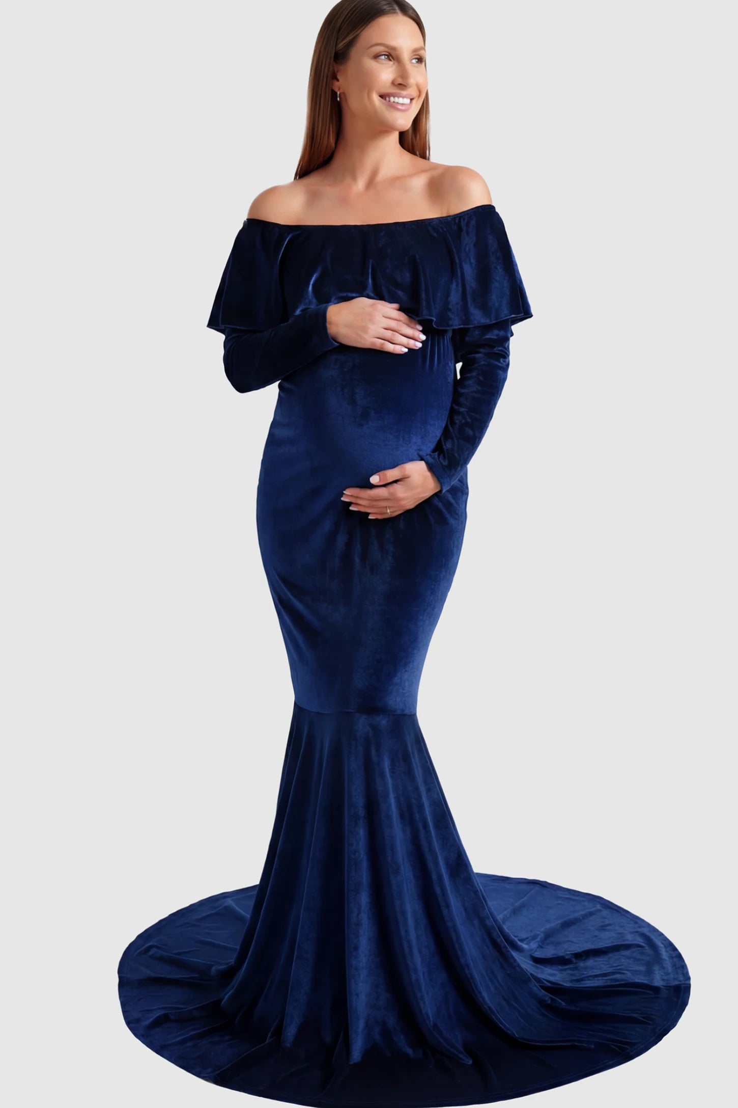 Velvet Off-the-Shoulder Maternity Mermaid Gown in Dark Blue featuring a ruffled neckline and long sleeves on a pregnant model posing front.