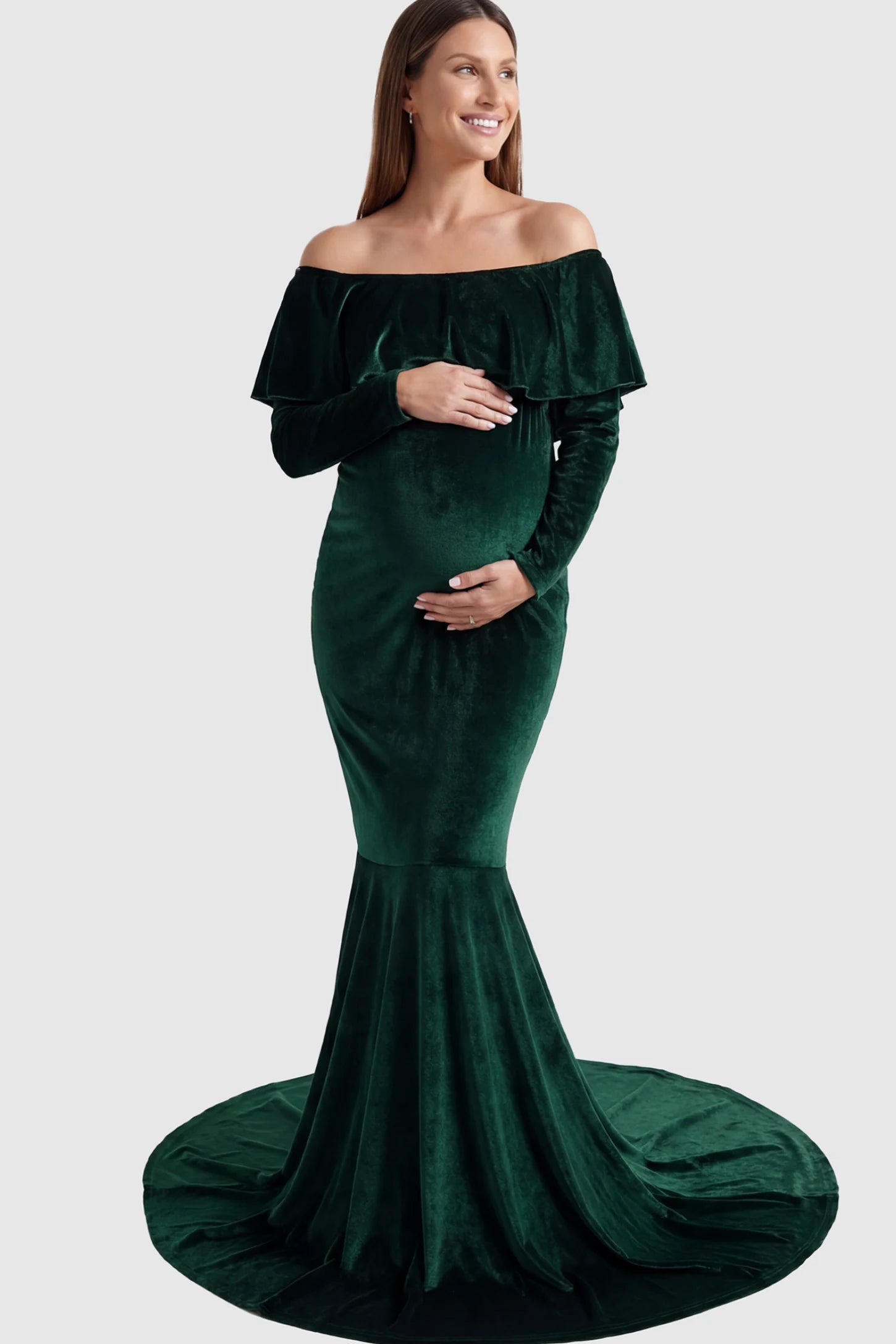 Velvet Off Shoulder Long Sleeve Maternity Mermaid Gown Velvet Off-the-Shoulder Maternity Mermaid Gown in Green featuring a ruffled neckline and long sleeves on a pregnant model posing front.