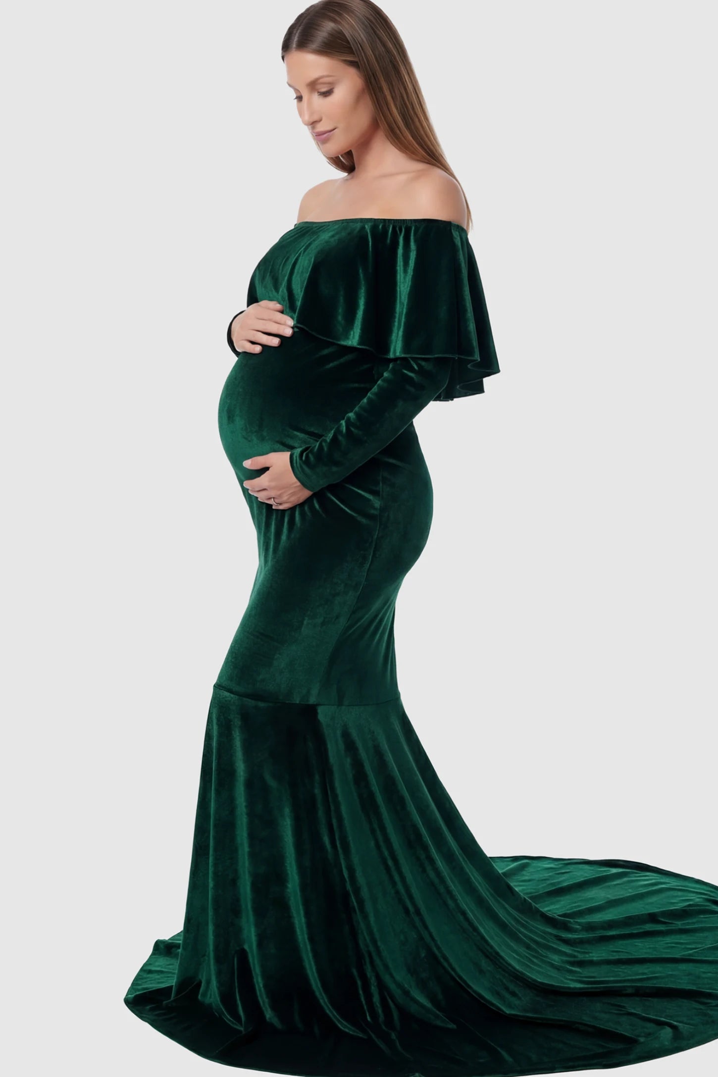 Velvet Off Shoulder Long Sleeve Maternity Mermaid Gown Velvet Off-the-Shoulder Maternity Mermaid Gown in Green featuring a ruffled neckline and long sleeves on a pregnant model showing side.