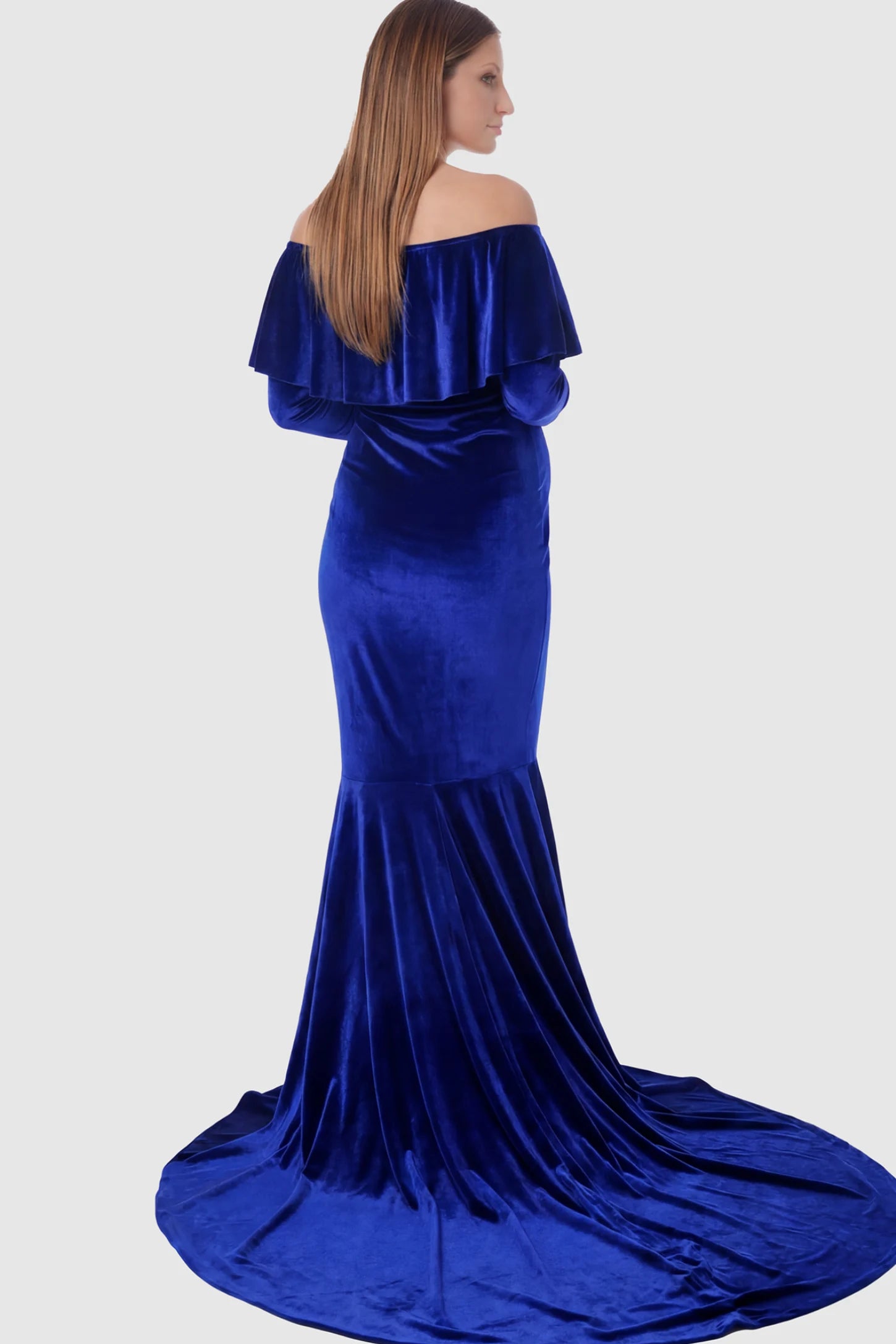 Velvet Off Shoulder Long Sleeve Maternity Mermaid Gown Velvet Off-the-Shoulder Maternity Mermaid Gown in Rainbow Blue featuring a ruffled neckline and long sleeves on a pregnant model showing back.