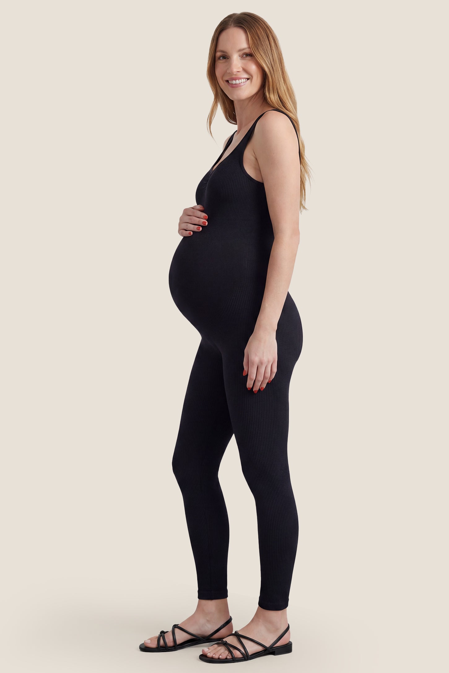 Side view of black scoop neck sleeveless ribbed bodycon maternity jumpsuit with bump-friendly fit